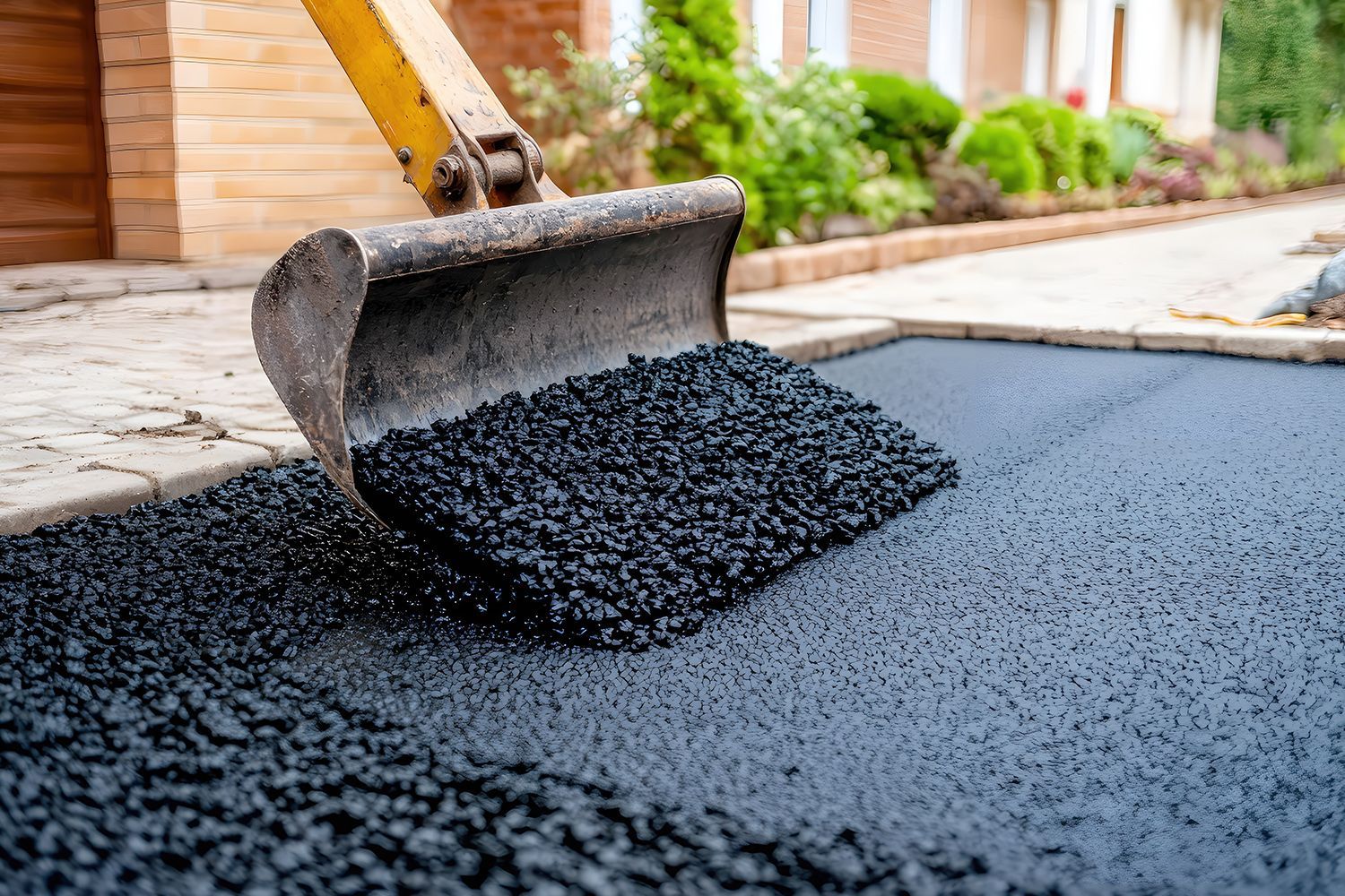 Excavator bucket spreading fresh black asphalt on a driveway.