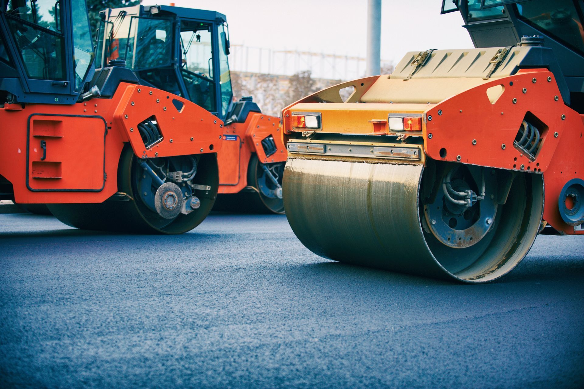 Two orange road rollers compacting fresh asphalt on a paved road. Two orange road rollers compacting fresh asphalt on a paved road.