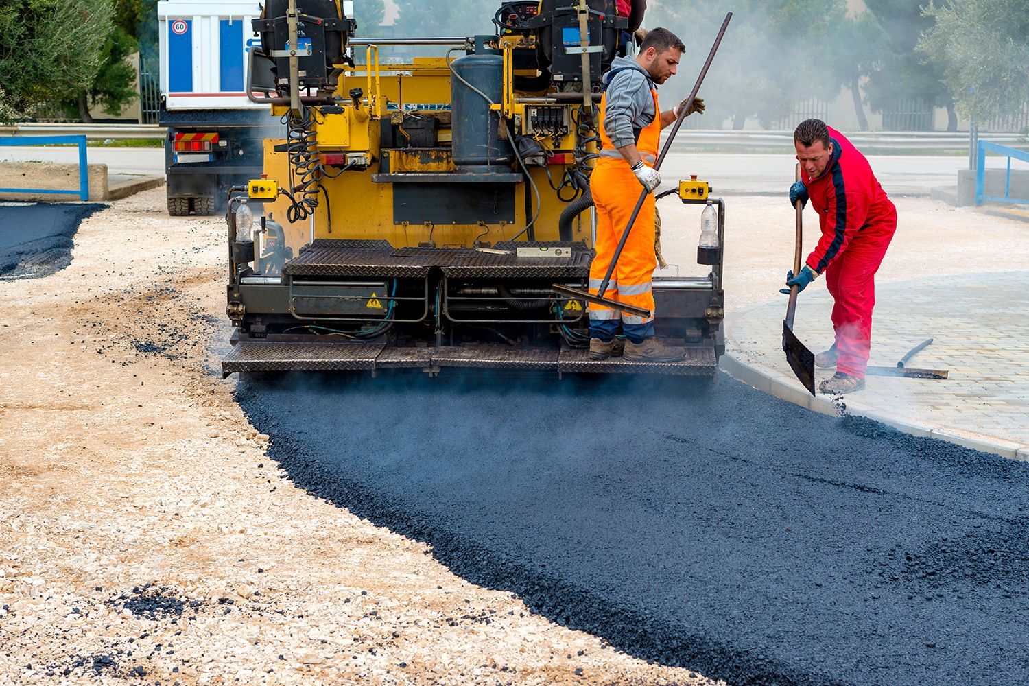 Asphalt paving machine laying blacktop with two workers nearby.