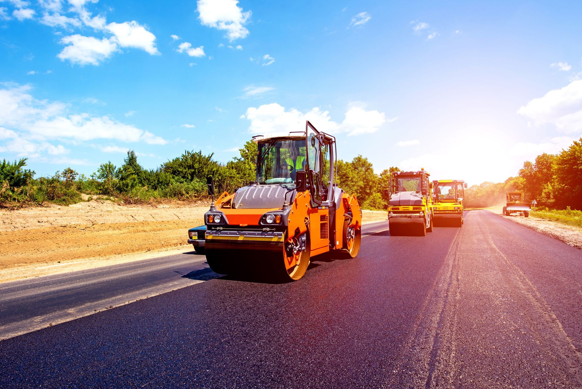 Road rollers compacting fresh asphalt on a sunny day.