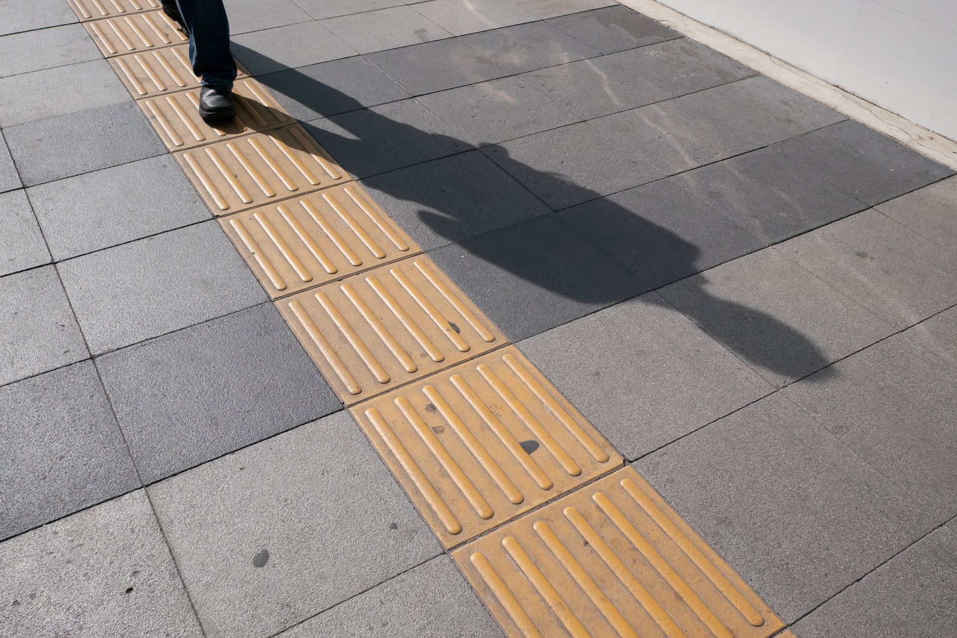 Person walking on a sidewalk with tactile paving for the visually impaired. Person walking on a sidewalk with tactile paving for the visually impaired.