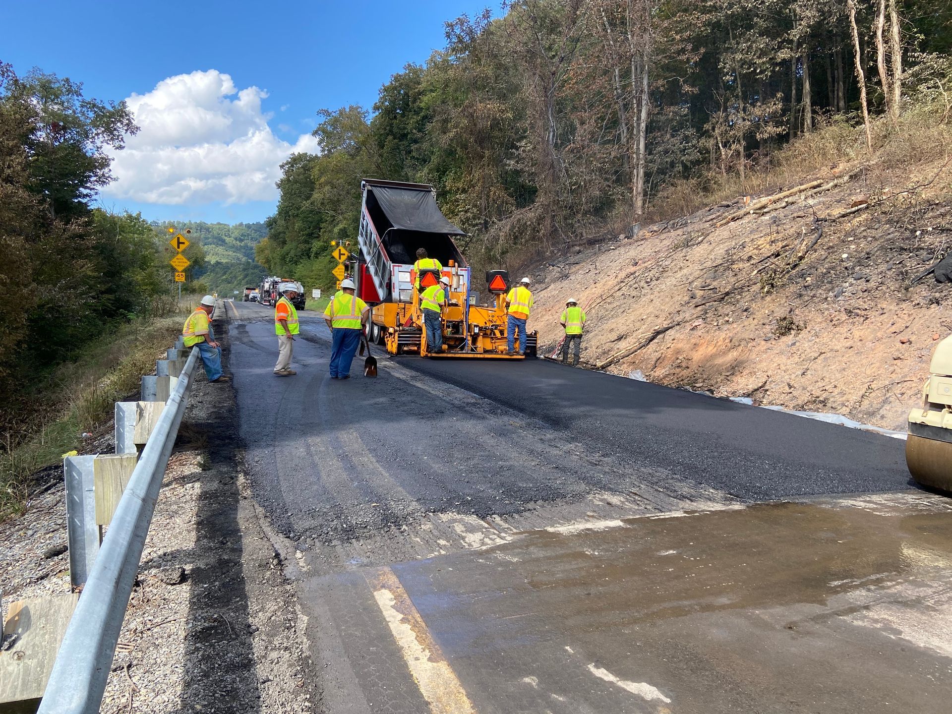 Road crew paving asphalt on a highway next to a wooded hillside. Road crew paving asphalt on a highway next to a wooded hillside.