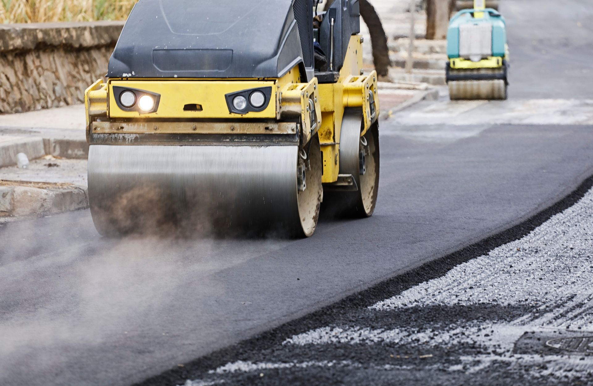 Road roller compacting fresh asphalt on a road, with another roller in the background. Road roller compacting fresh asphalt on a road, with another roller in the background.