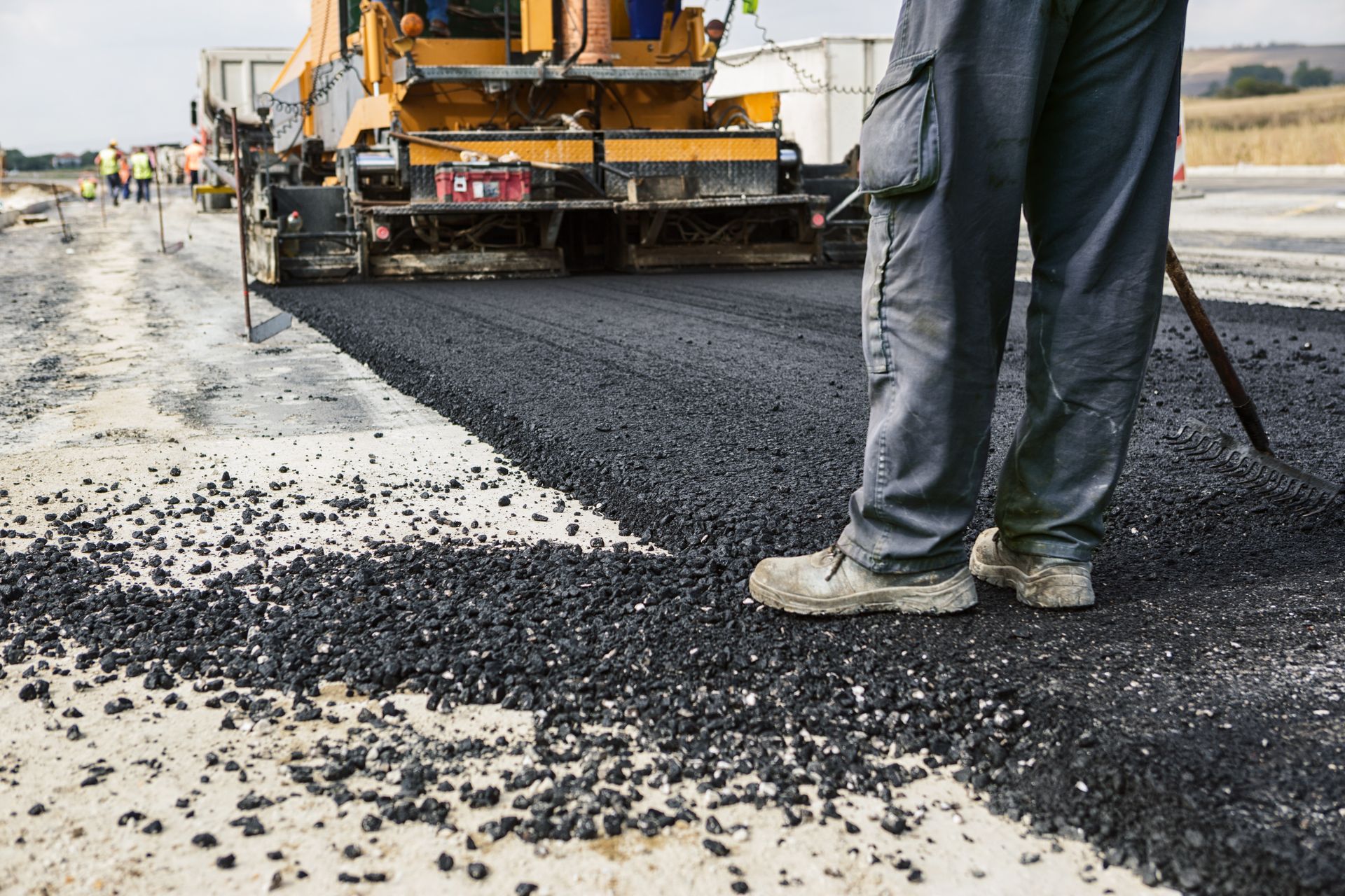 Road construction: worker standing next to asphalt paving machine, laying fresh black asphalt on a road. Road construction: worker standing next to asphalt paving machine, laying fresh black asphalt on a road.