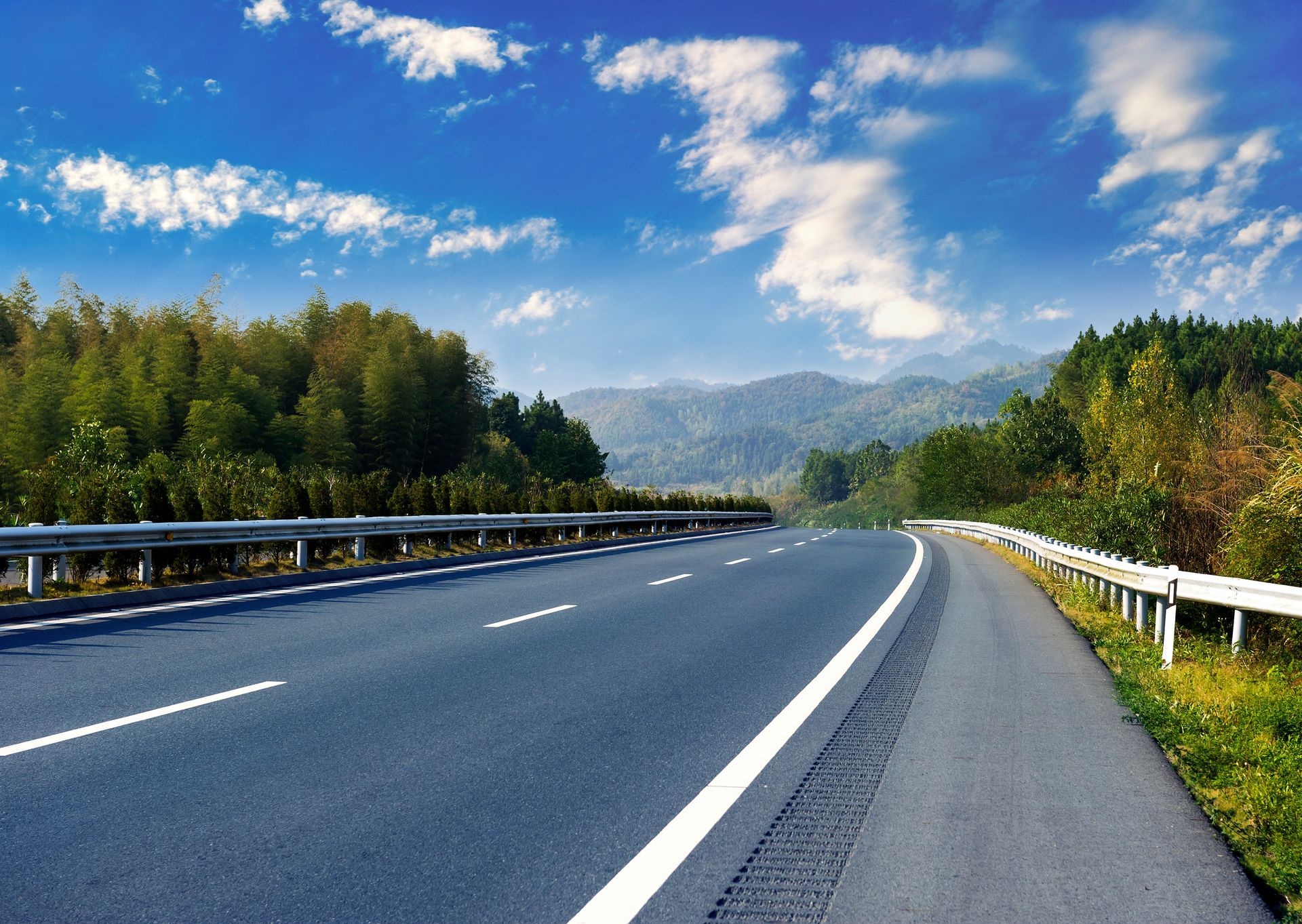Road winding through a lush green landscape under a blue sky with fluffy clouds.