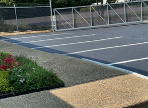 Road workers in orange coveralls smoothing asphalt on a road.