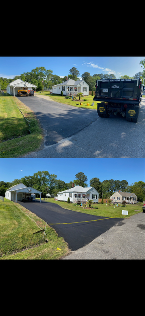 Asphalt driveway leading to a house with a black garage door on a sunny day.
