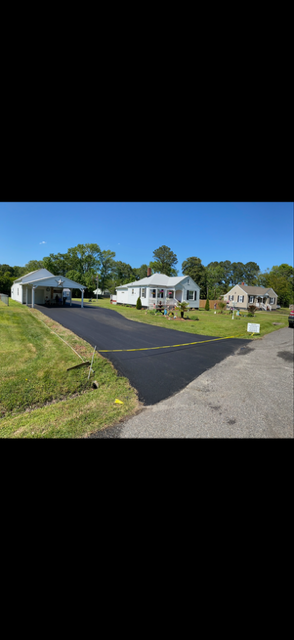 Newly paved black asphalt driveway in front of a house with brown garage doors.