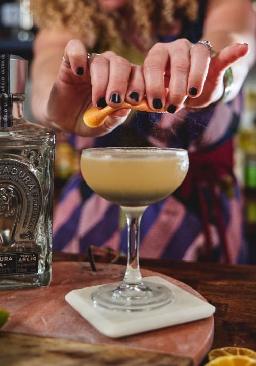 bartender squeezing an orange peel over a cocktail made with Herradura Anejo tequila