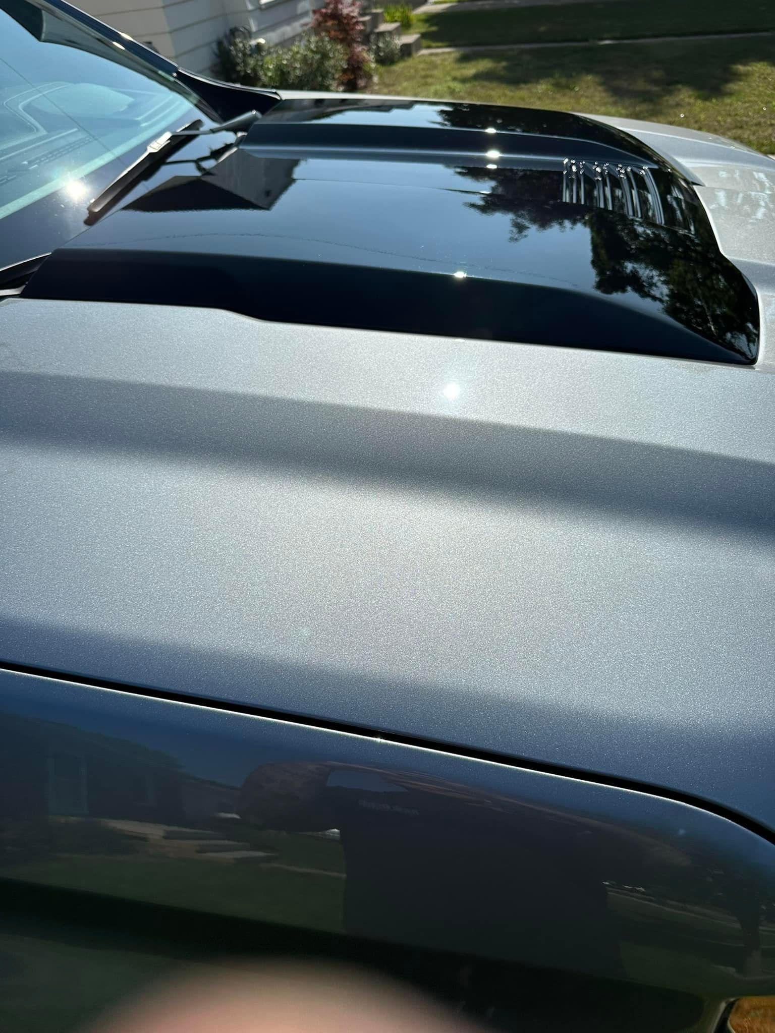 Close-up of a car hood with a black scoop. The hood is a silver-gray color.