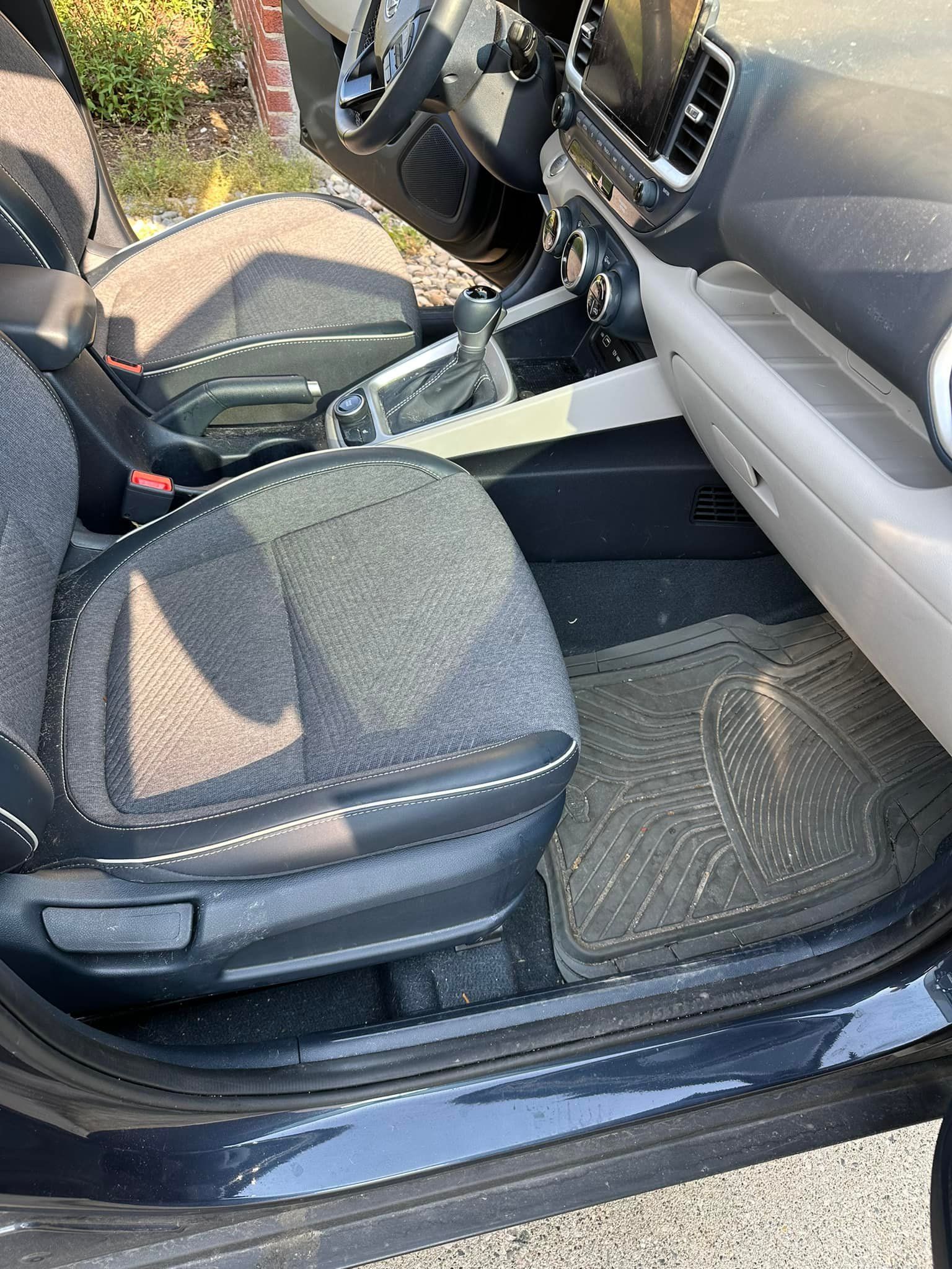 Interior of a car with a gray seat, black floor mat, and open door.