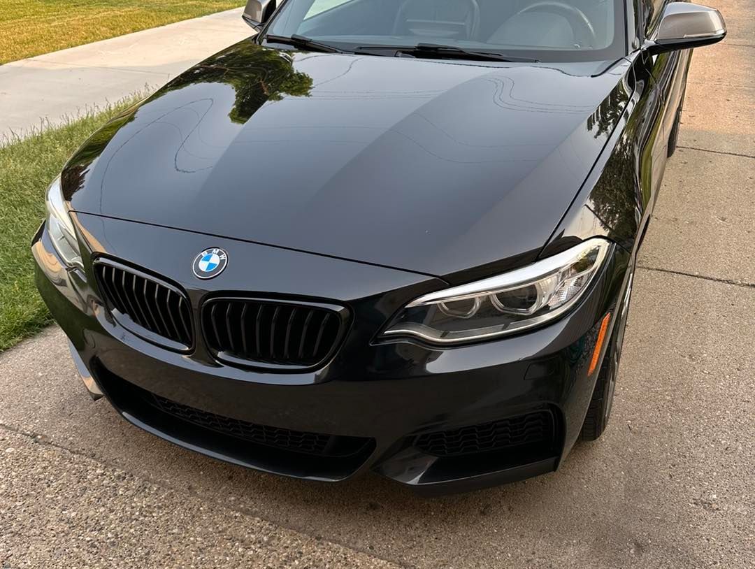 Black BMW coupe parked on a paved driveway with a grassy lawn in the background.