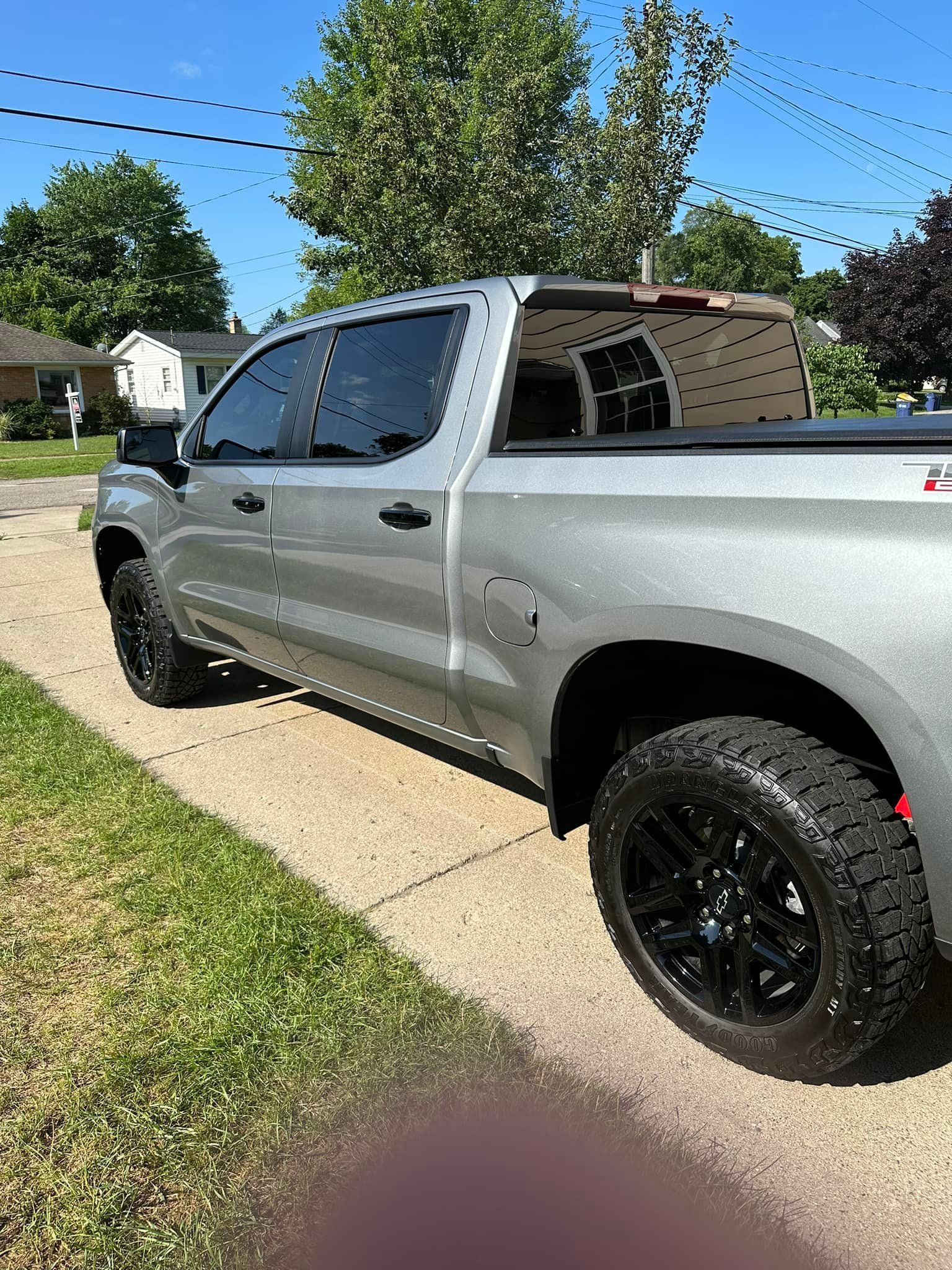 Silver pickup truck parked on a driveway, black wheels, against a backdrop of a residential neighborhood.