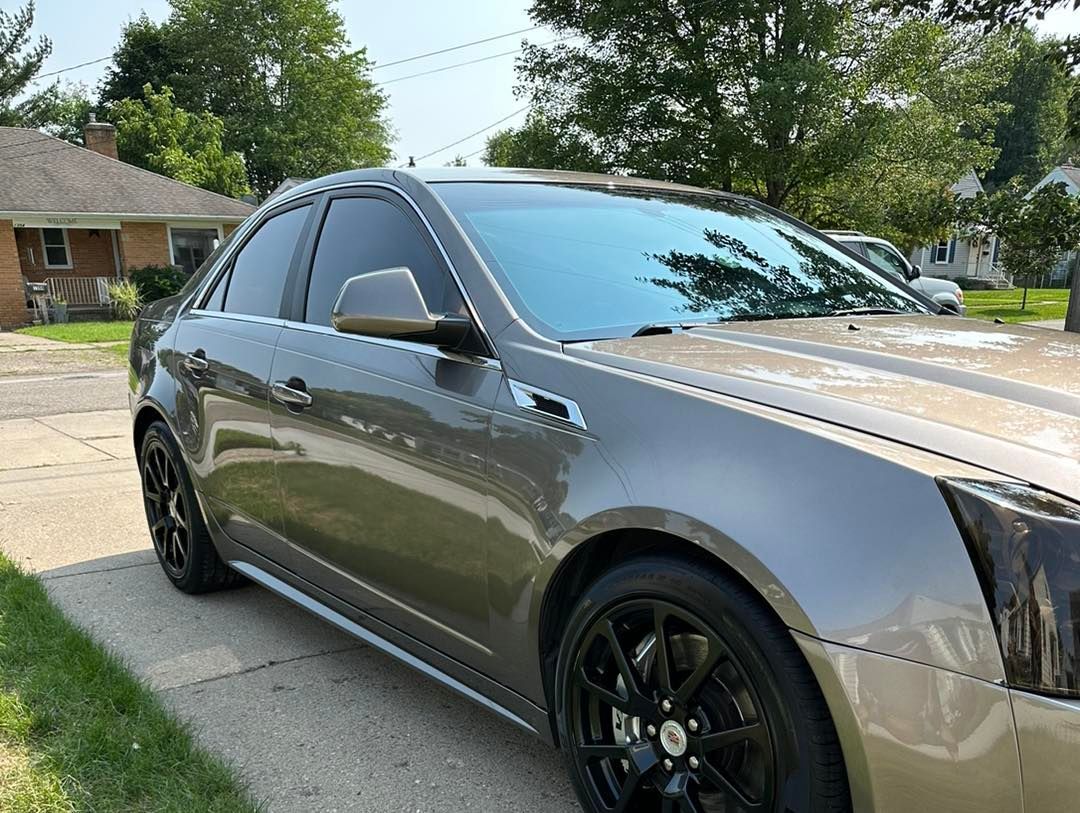Gray Cadillac CTS sedan with tinted windows, parked on a paved driveway in front of a house.