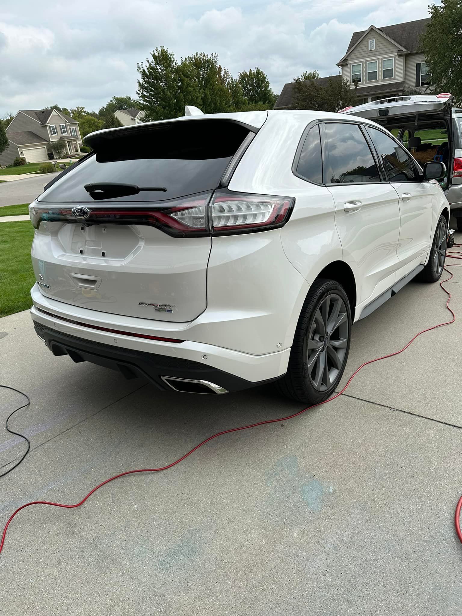 White Ford Edge SUV parked on a driveway with red wires.