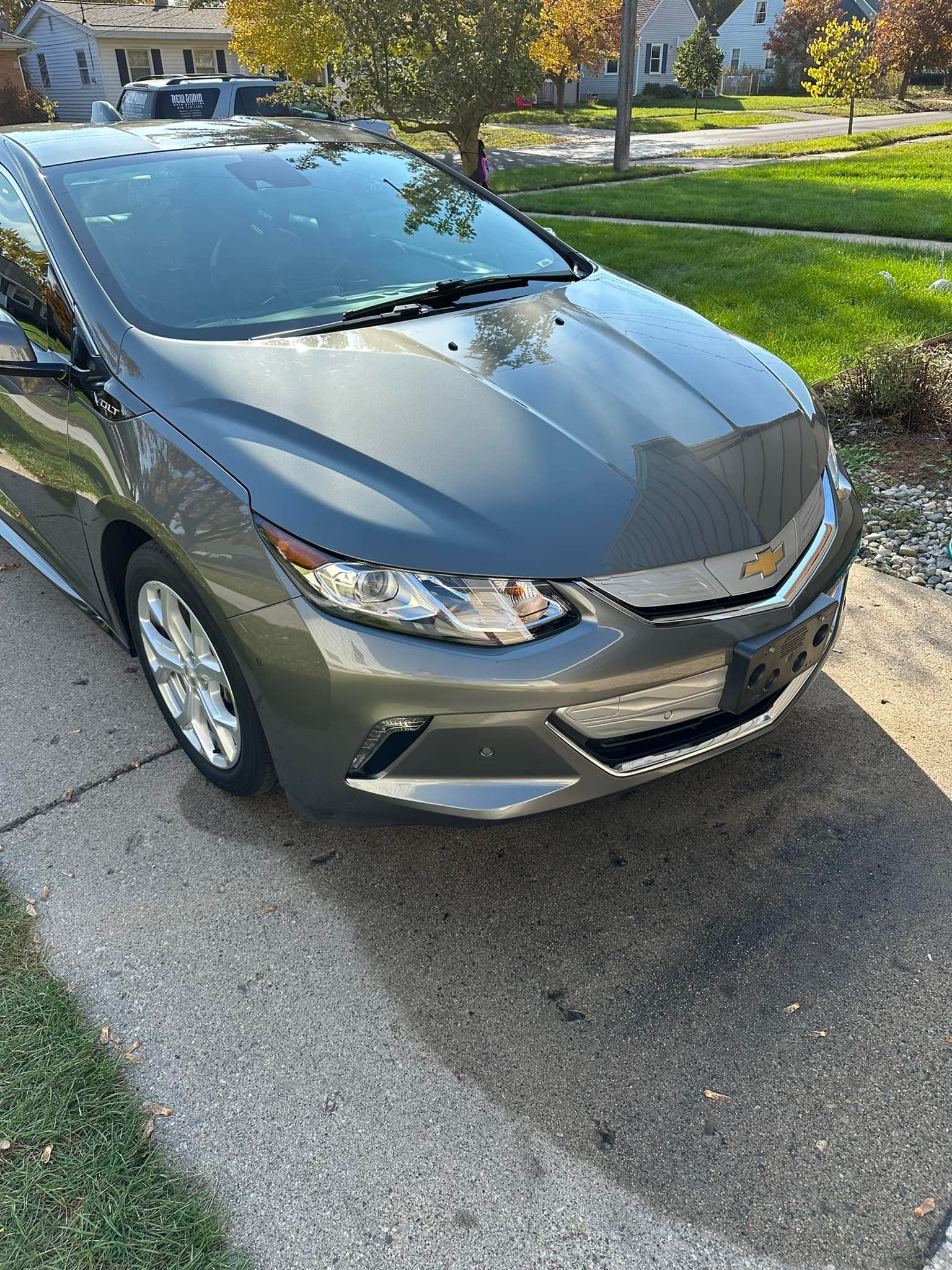 Gray Chevrolet Volt parked on a sidewalk next to a grassy lawn.