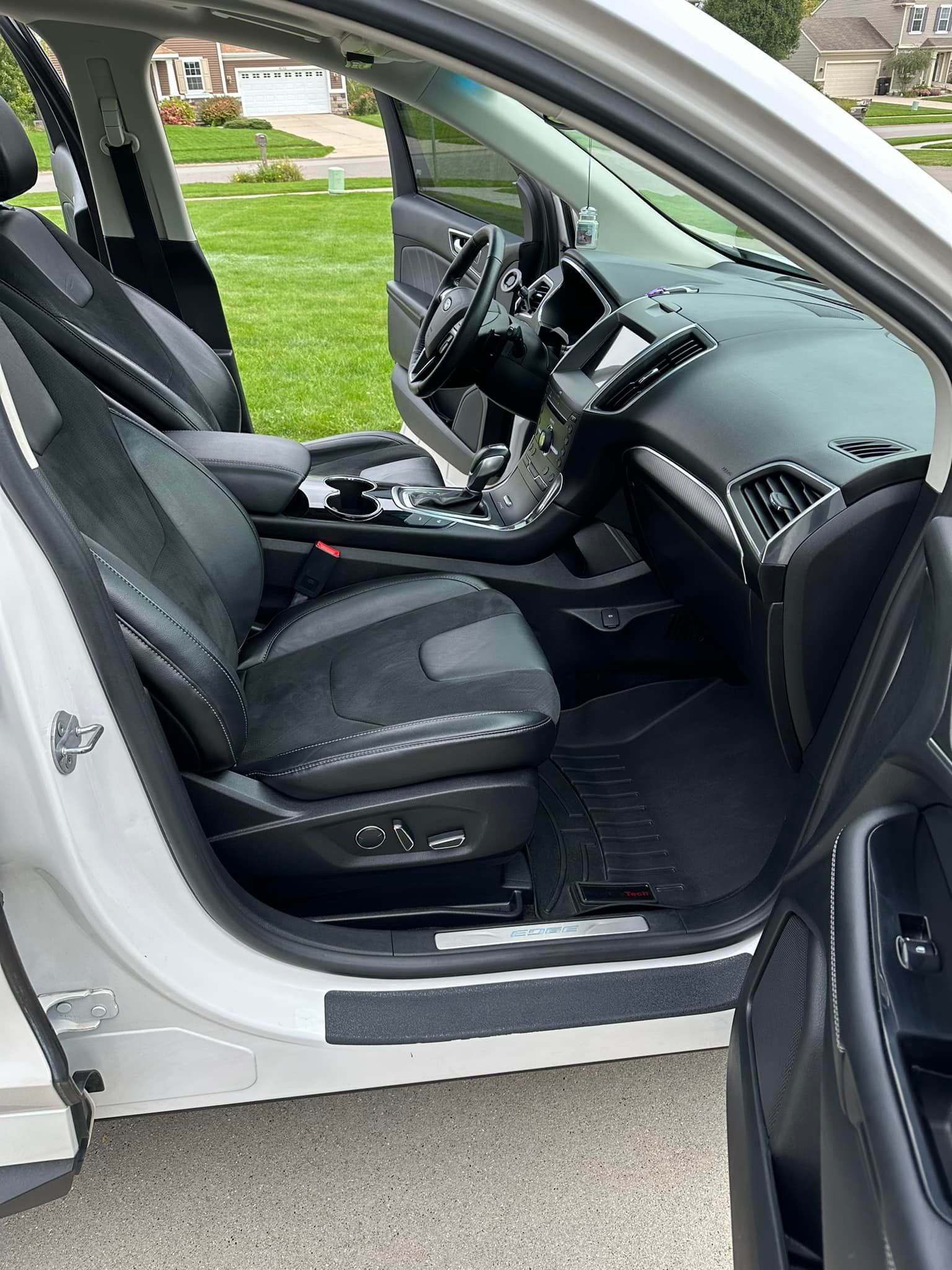 Interior view of a white car with black leather seats, door open.