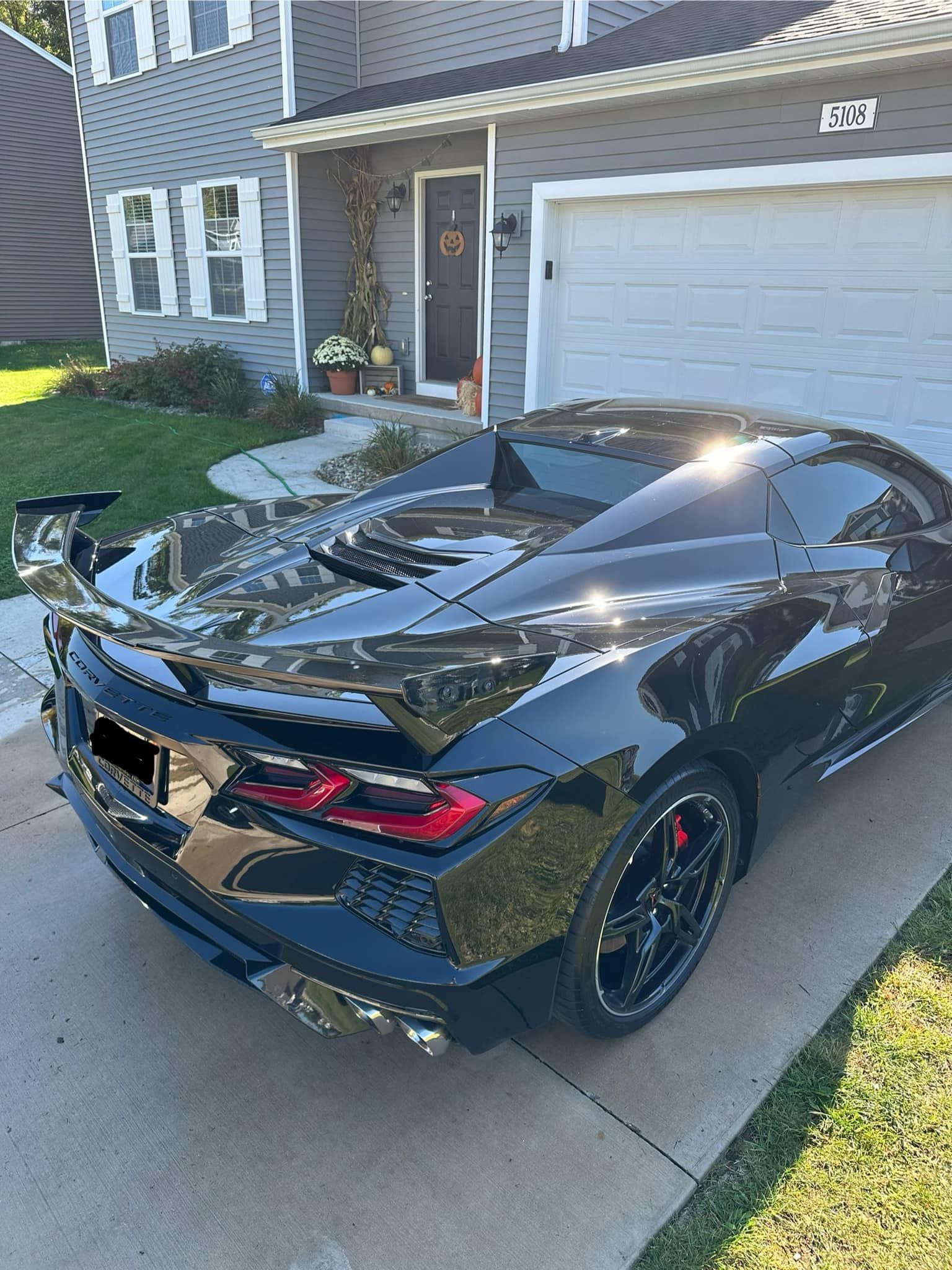 Black sports car parked on driveway in front of a house.