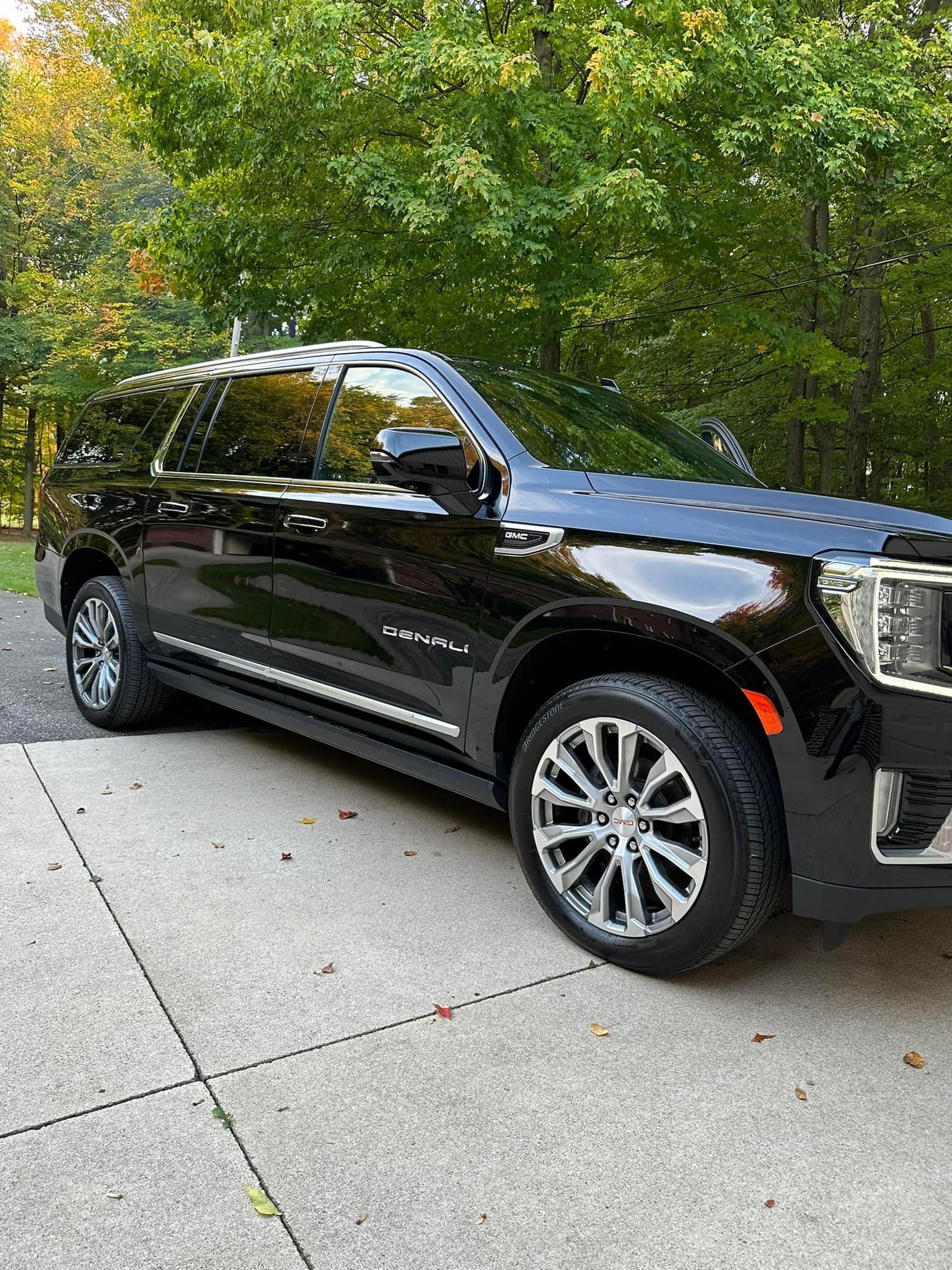 Black GMC Yukon SUV parked on a concrete driveway in front of trees.
