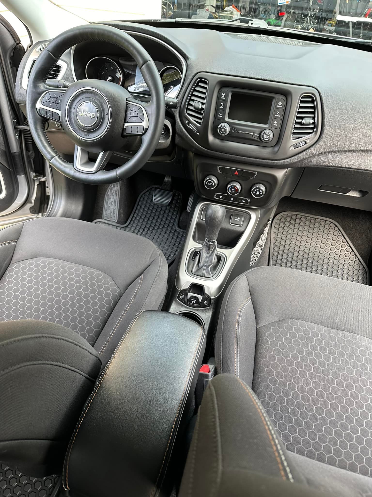 Interior view of a Jeep Compass with black steering wheel, dashboard, seats, and gear shift.