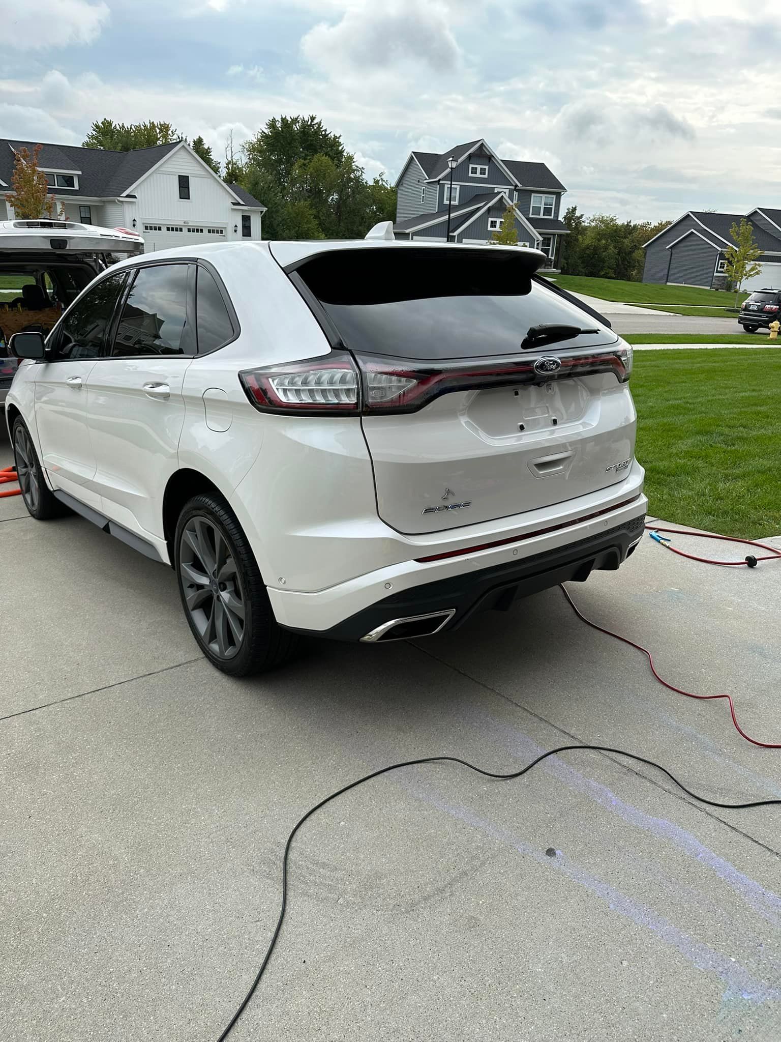 White Ford Edge SUV parked on a driveway with tinted windows, gray wheels, and a residential background.