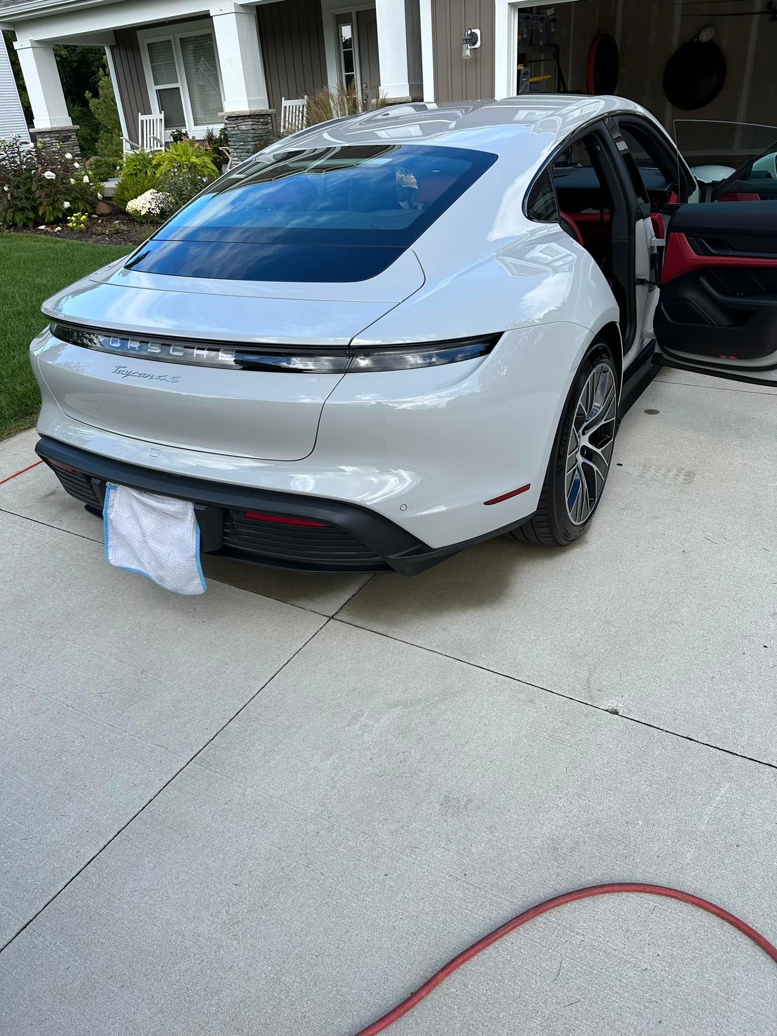 White Porsche Taycan sedan with a red interior parked on a driveway, door open.