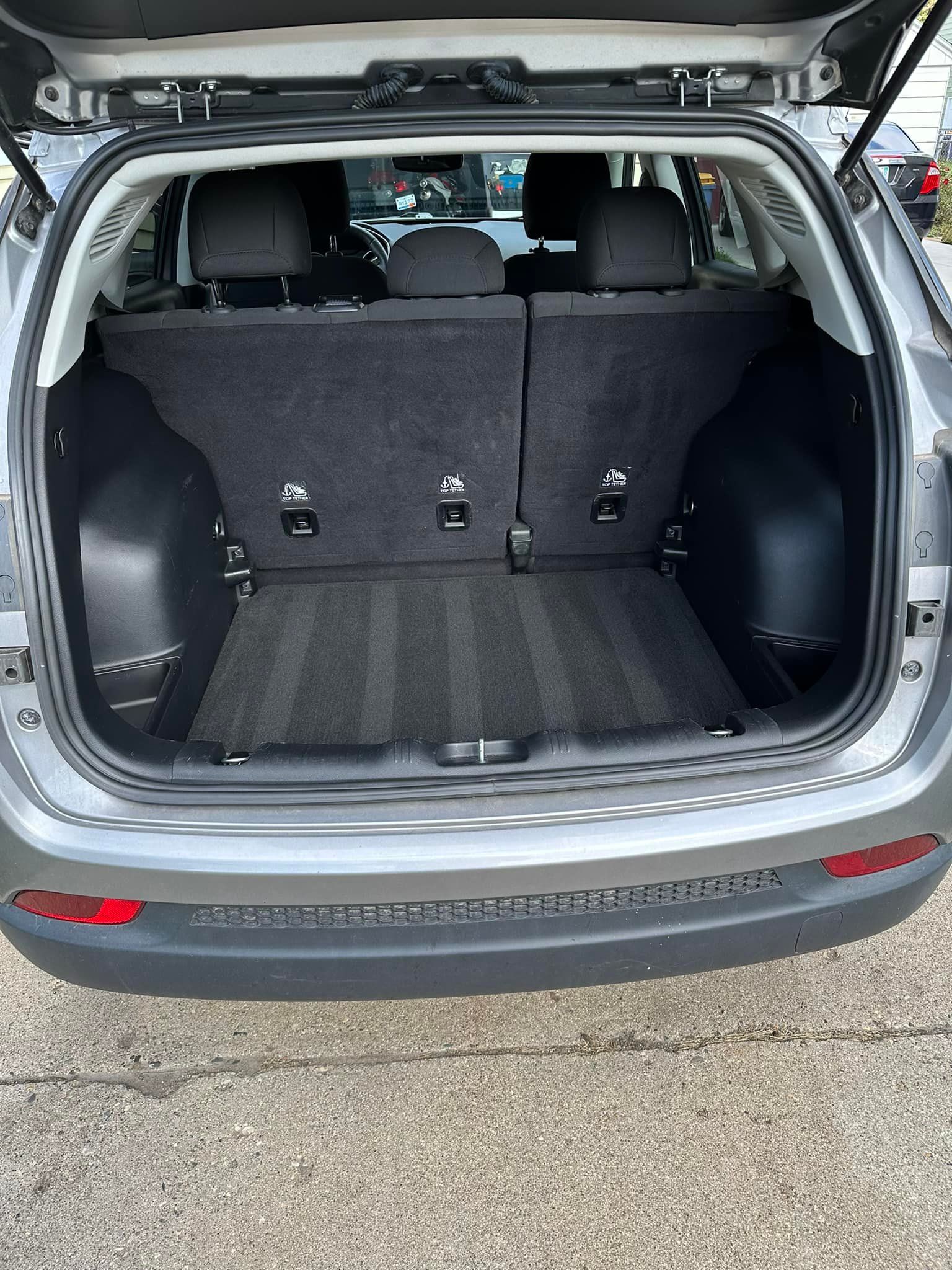 Open trunk of a silver Jeep Compass. The back seats are up, revealing a cargo area with black carpet.