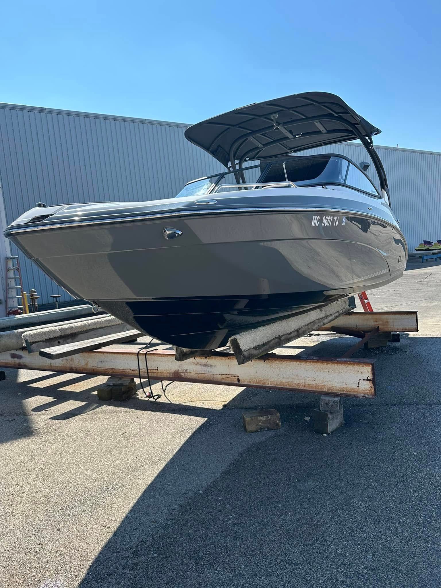 Gray motorboat on a trailer, under a black canopy, against a blue sky.