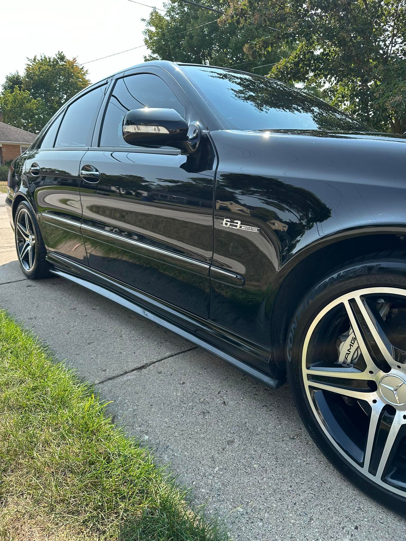 Black Mercedes-Benz sedan parked on a sidewalk with tinted windows and custom wheels.