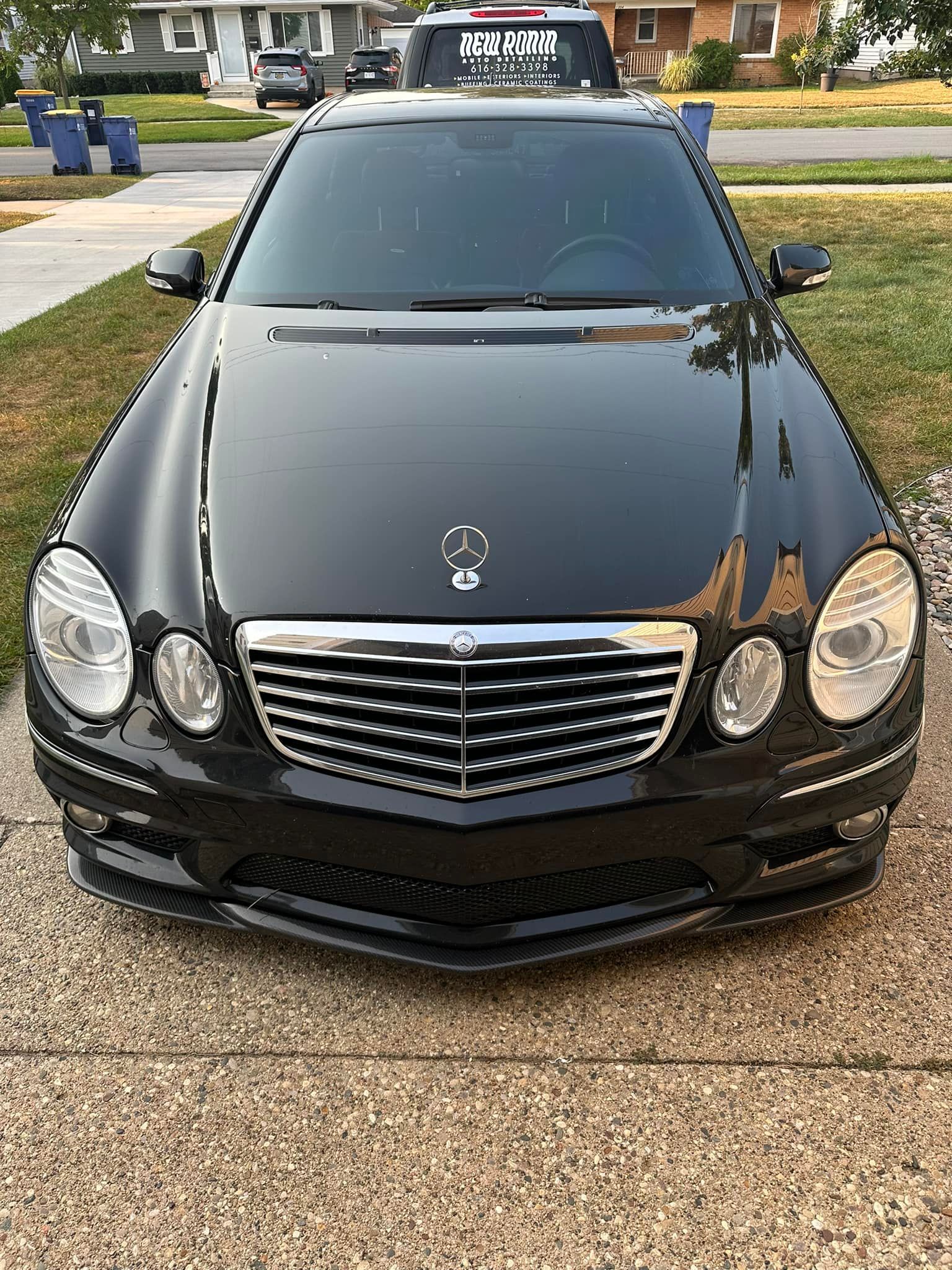 Black Mercedes-Benz sedan parked on a driveway, viewed from the front. Sunny outdoor setting.