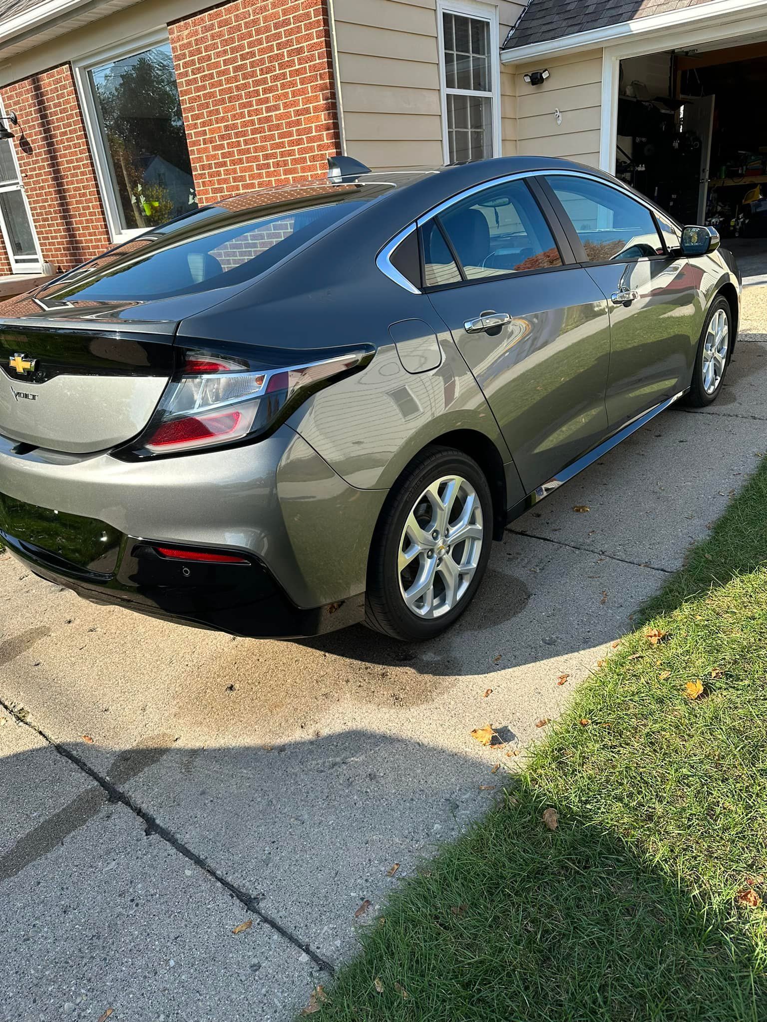 Gray Chevy Volt parked on a paved driveway next to green grass. Red brick house in background.