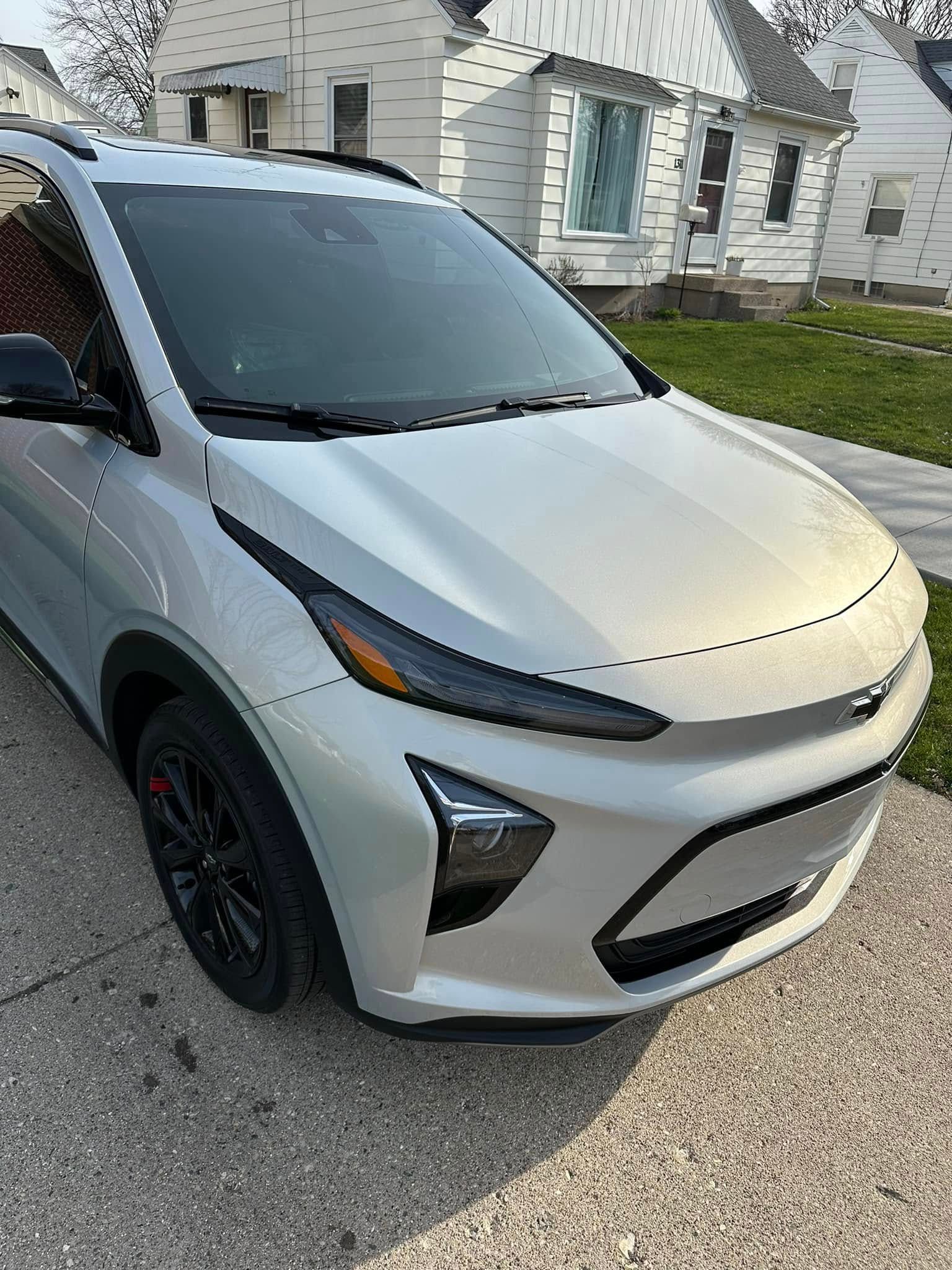 Silver Chevy Bolt EV parked on a driveway in front of a house.