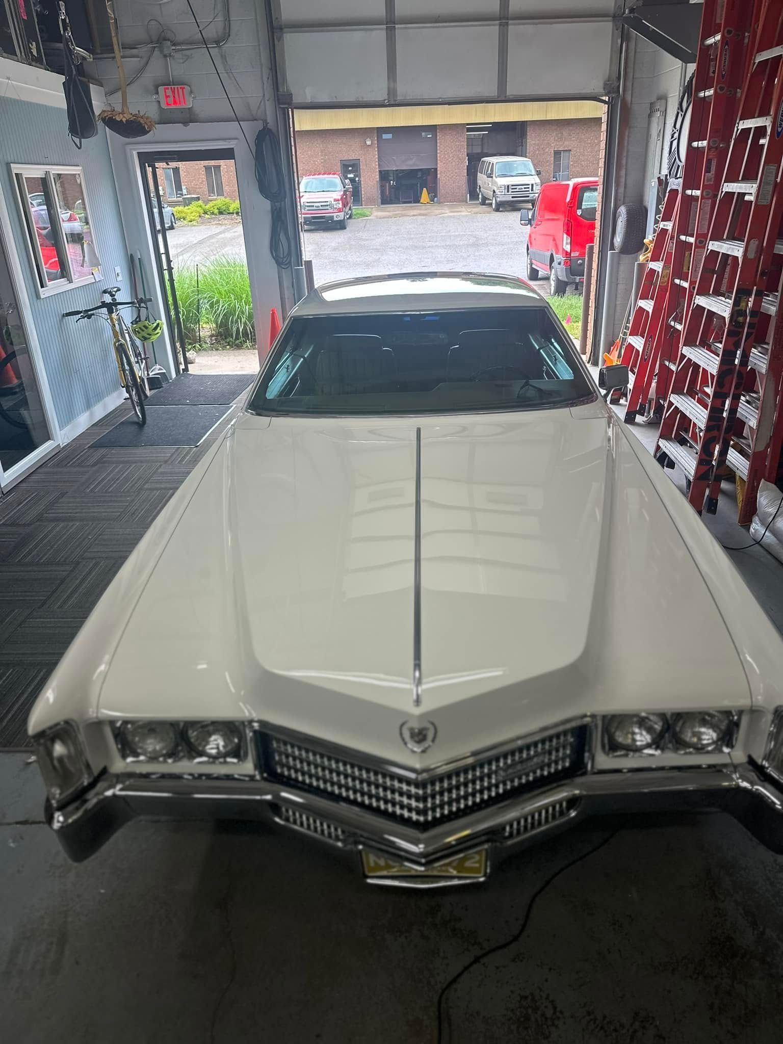 White classic Cadillac car parked inside a garage, open door, several other vehicles visible.