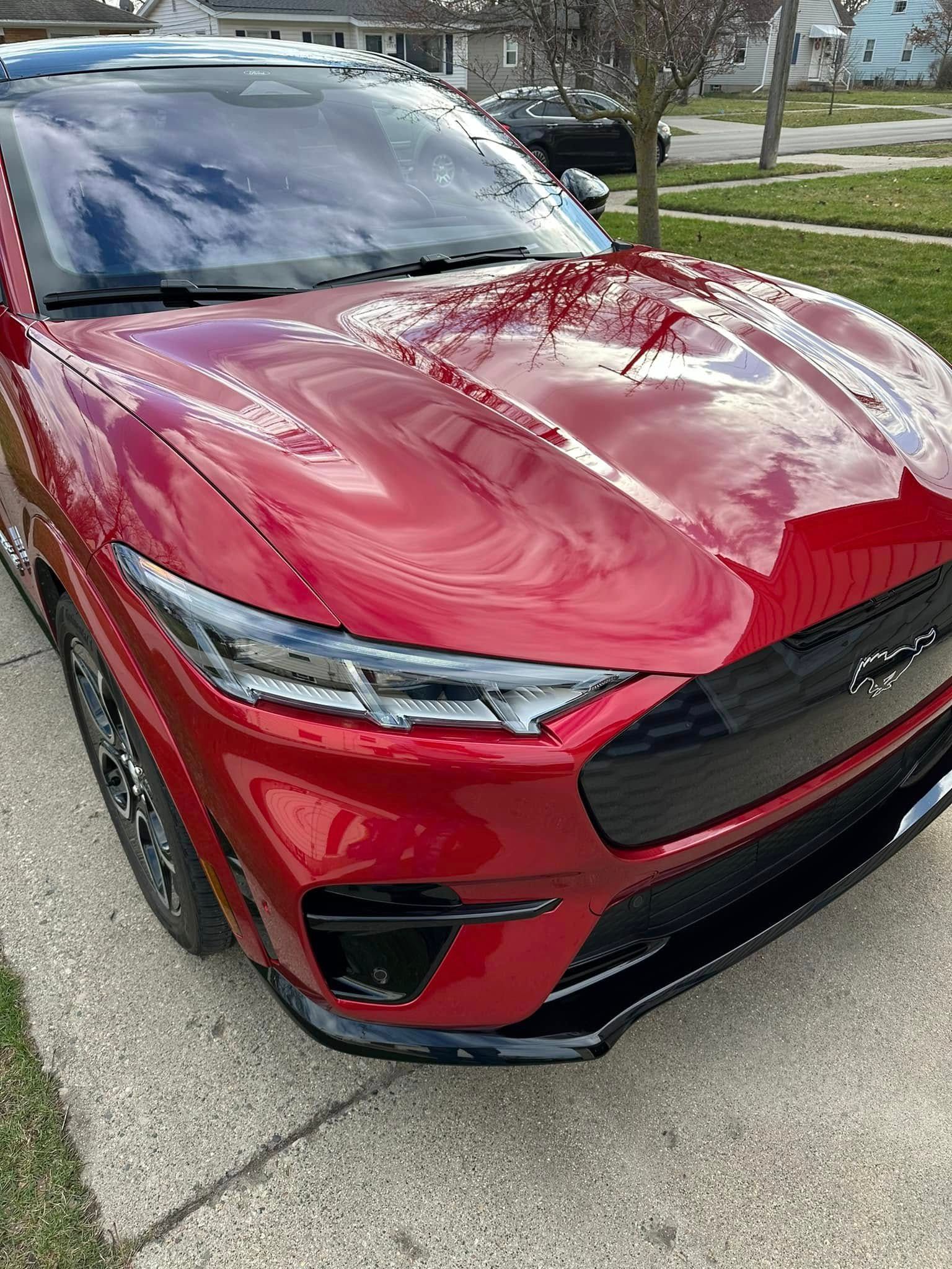 Red Ford Mustang Mach-E electric vehicle parked on a driveway, daytime.