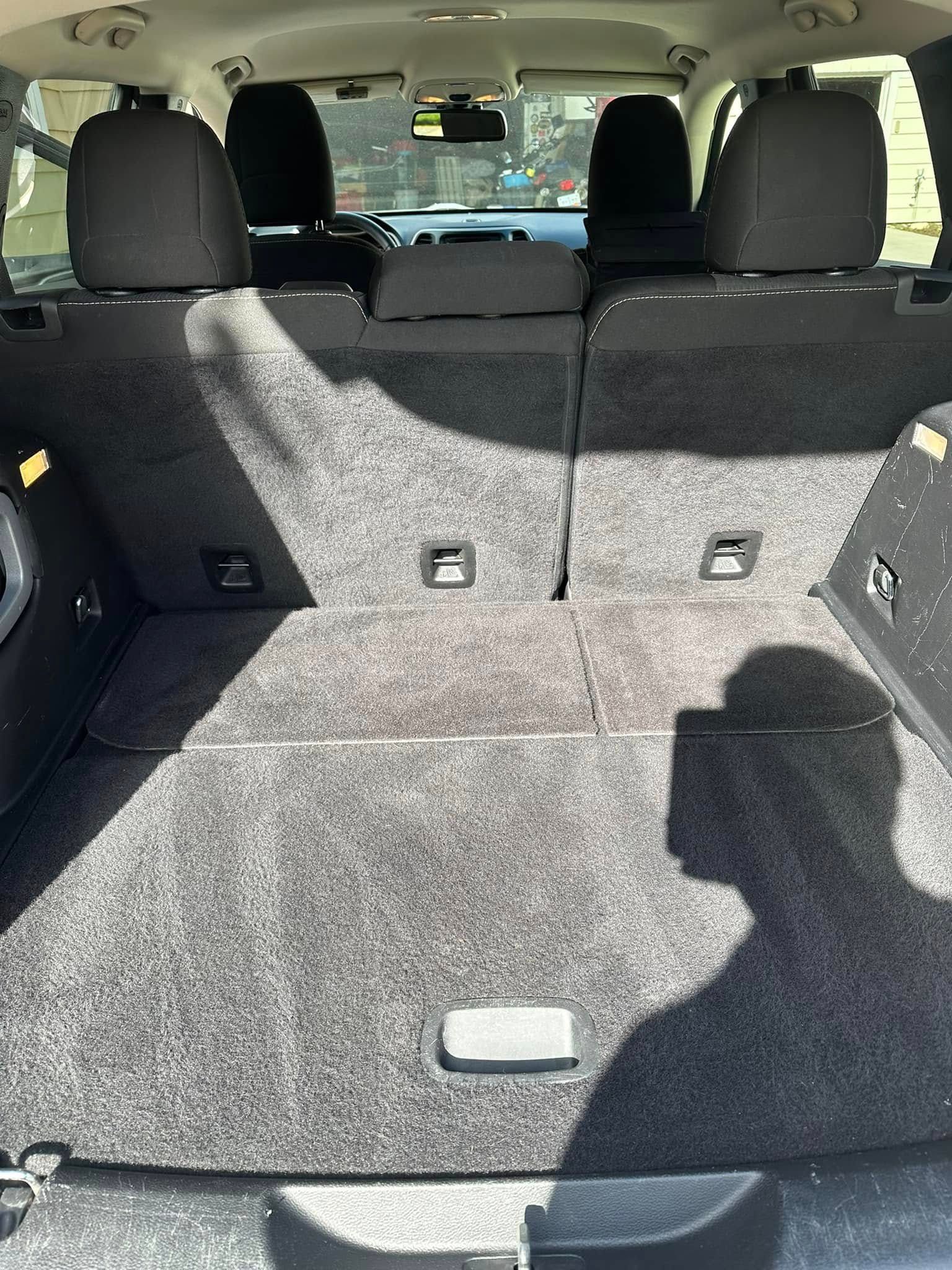 Interior of a car's cargo area. Gray carpet, black seats visible. A shadow is cast across the area.
