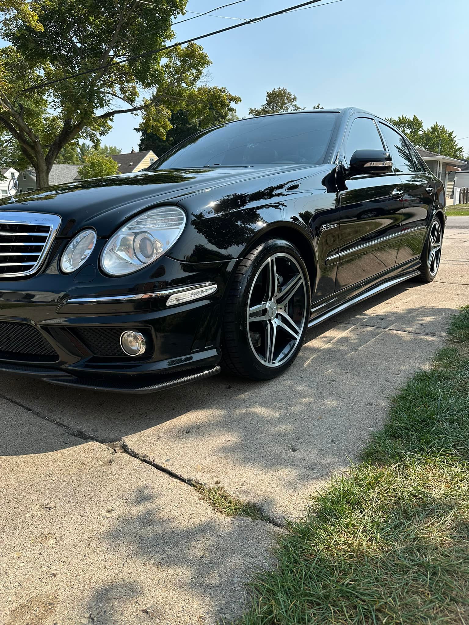 Black Mercedes-Benz sedan parked on a driveway, with tinted windows and custom wheels.