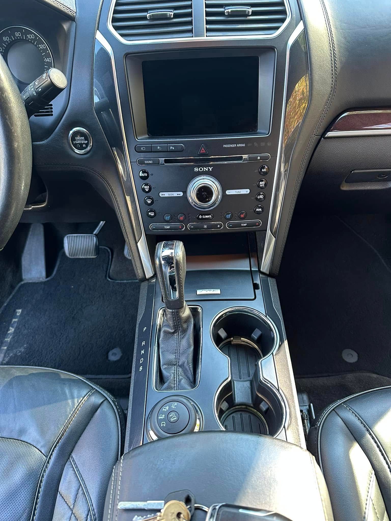 Interior view of a car dashboard and center console with gear shift, cup holders, and infotainment screen.