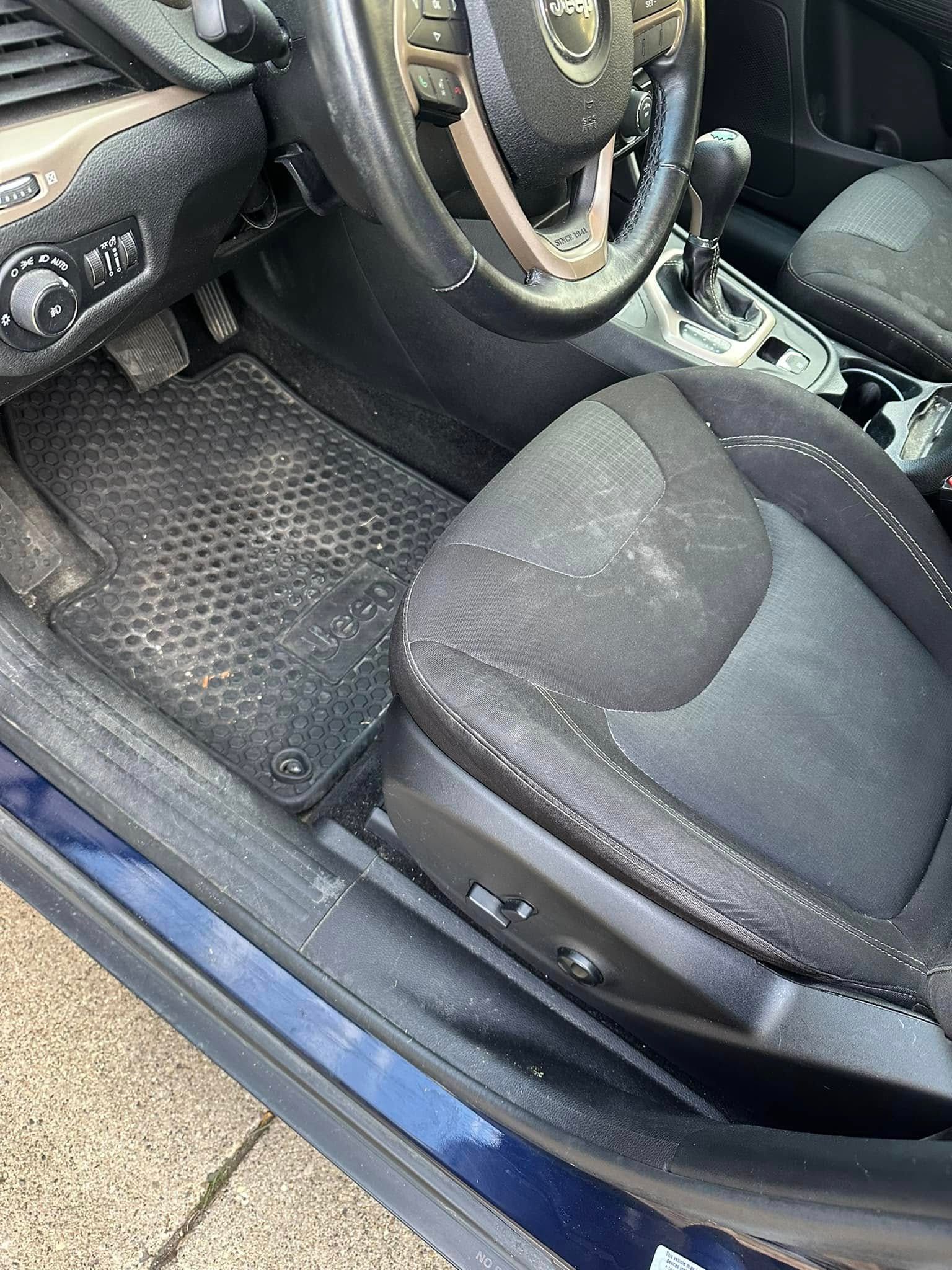 Interior view of a car with a black steering wheel, seat, and floor mat.