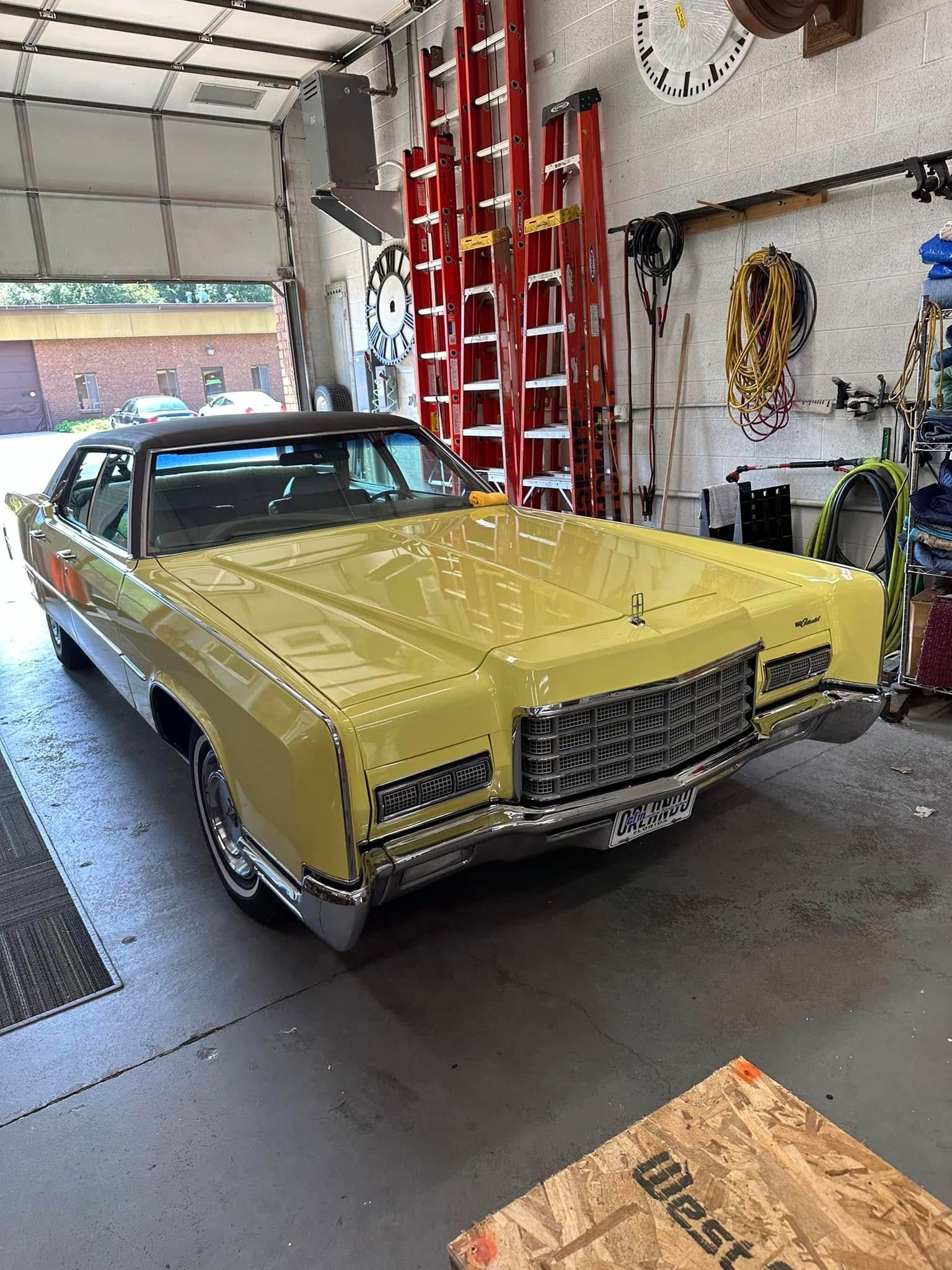 Yellow classic car parked inside a garage, with red ladders and tools visible.