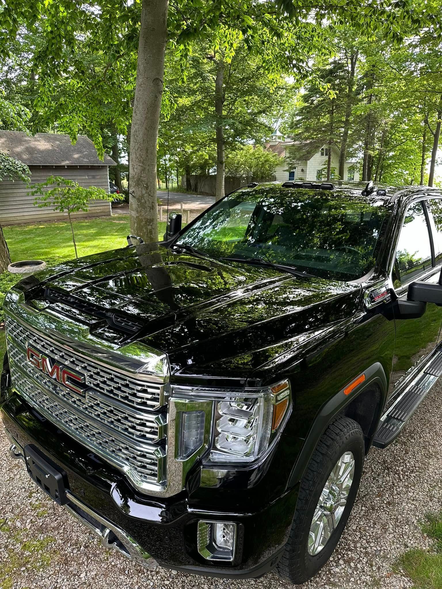 Black GMC truck parked outdoors with trees in the background. Shiny grill and chrome accents visible.