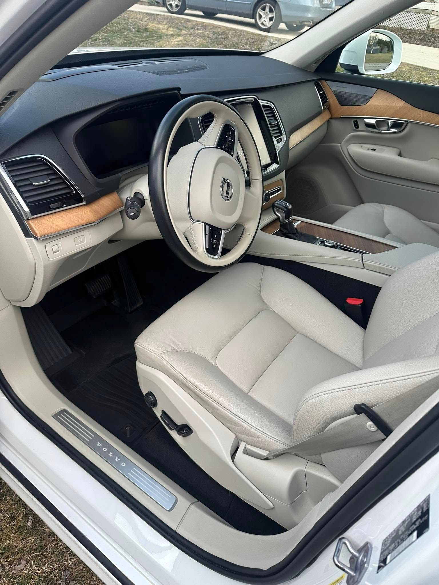 White Volvo SUV interior with cream-colored leather seats, wooden trim, and a black dashboard.