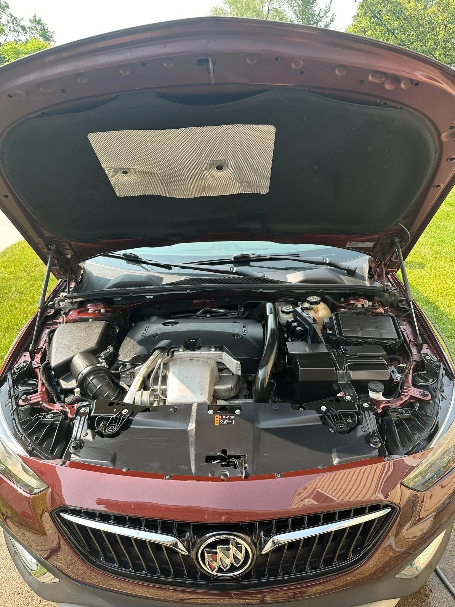 Burgundy Buick car engine bay open, showing engine and under-hood insulation.