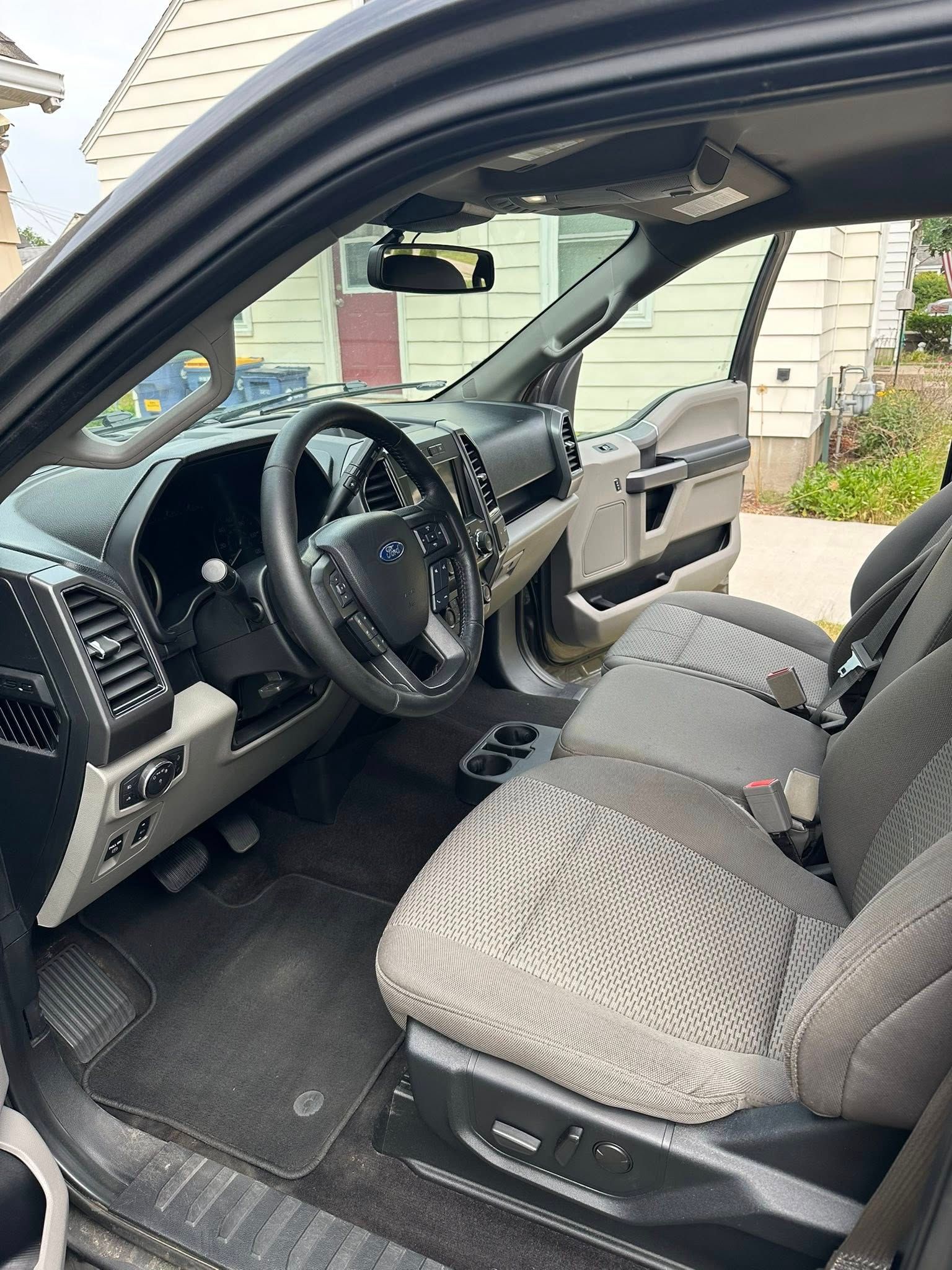 Interior of a gray Ford F-150 truck, showing the driver's side with black steering wheel and gray seats.