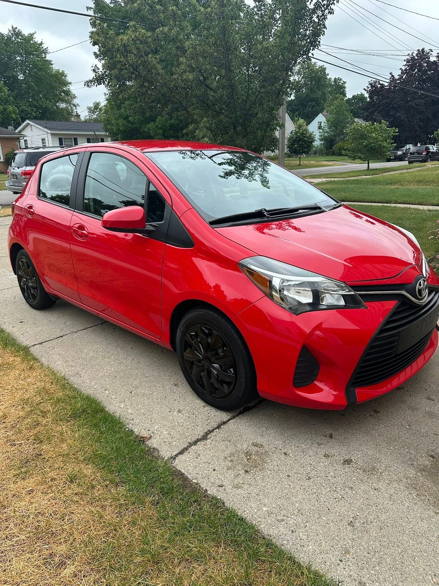 Red Toyota Yaris hatchback parked on a driveway with black wheels.