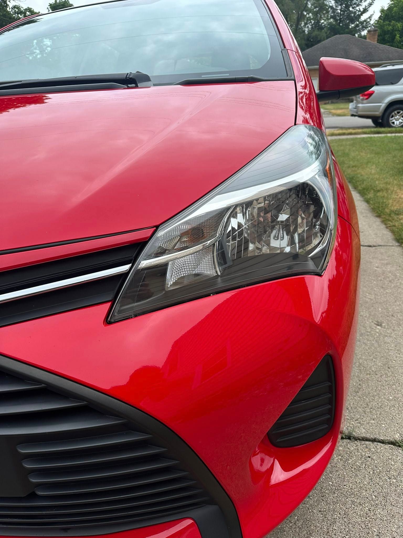 Red Toyota Yaris car front, shiny, on a driveway.