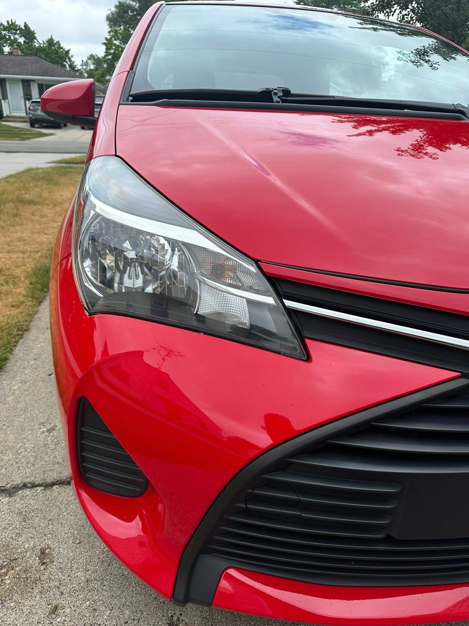 Red Toyota Yaris car front view with a black grill and headlights.