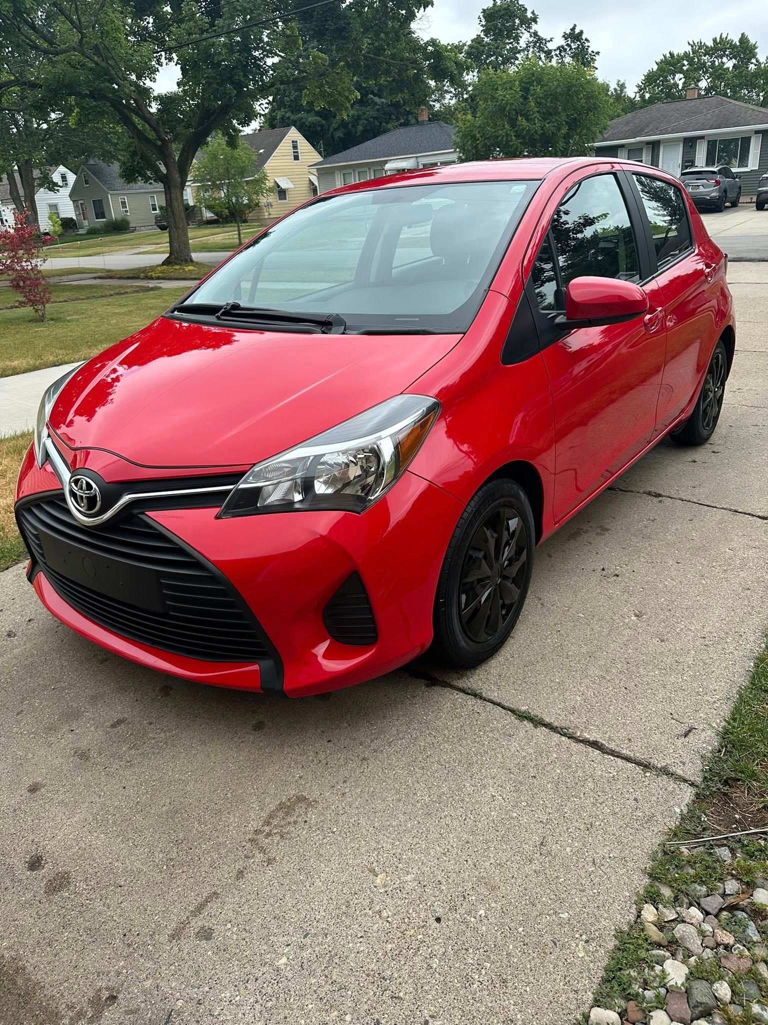 Red Toyota Yaris hatchback parked on a concrete driveway. Black wheels and black grill contrast the red paint.