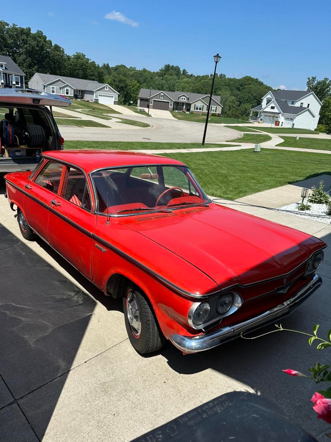 Red classic car parked in a driveway on a sunny day in a suburban neighborhood.