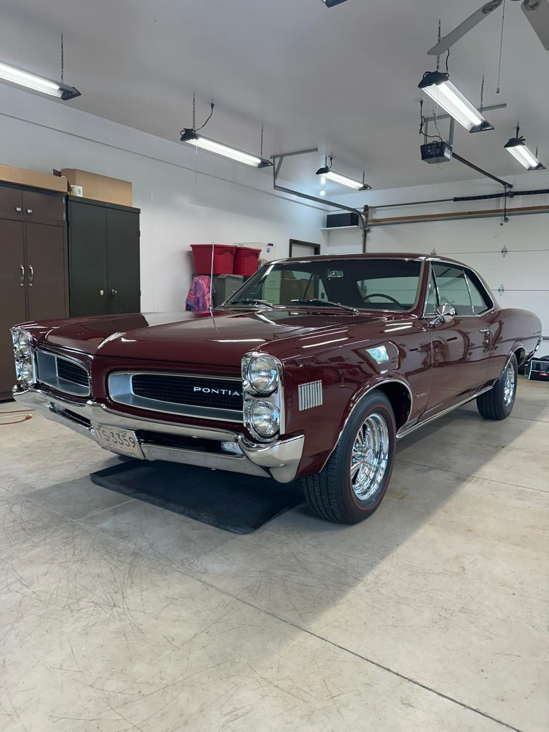 Maroon vintage Pontiac GTO coupe in a garage, shiny chrome wheels.