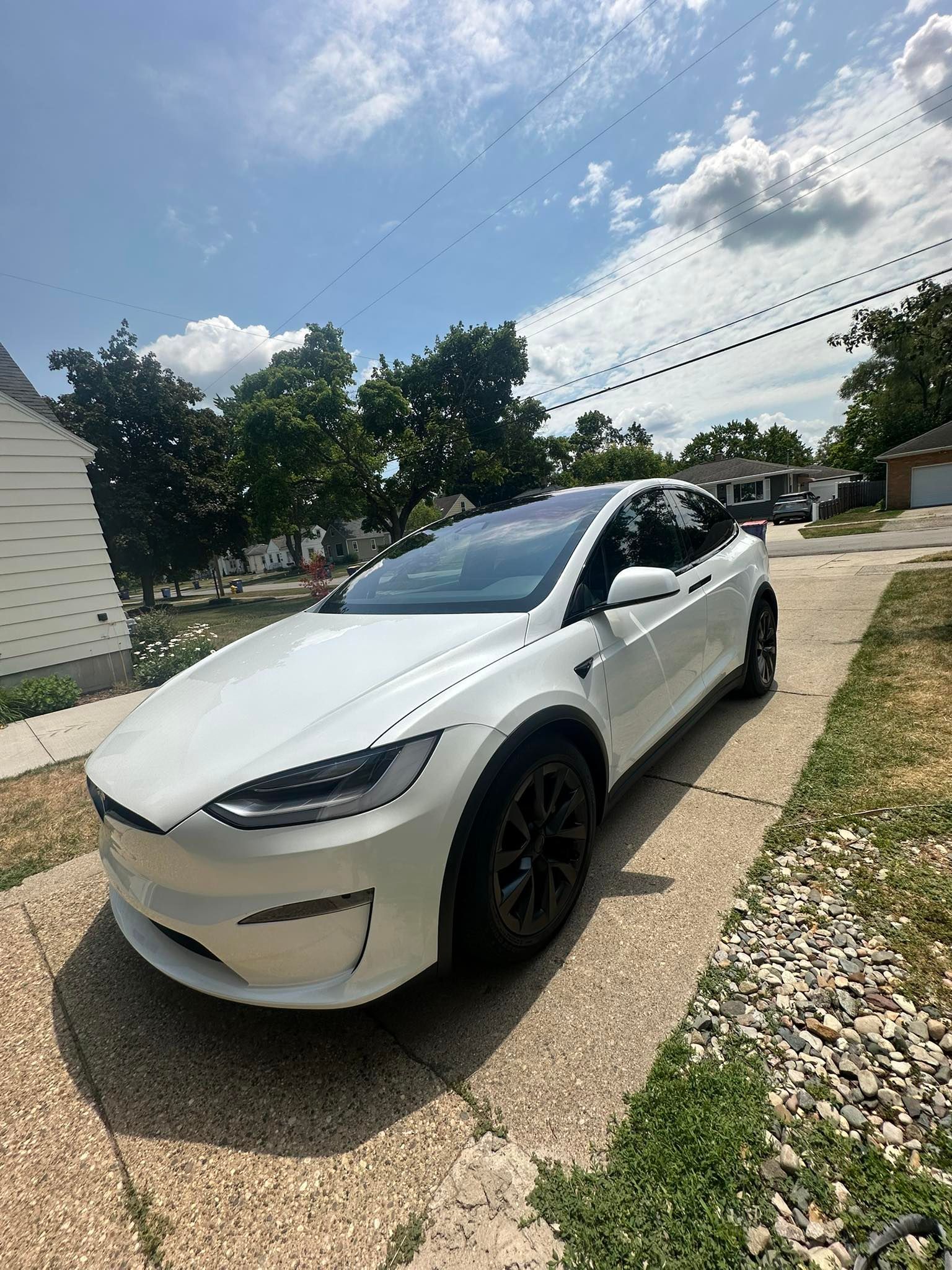 White Tesla Model X parked on a driveway on a sunny day.